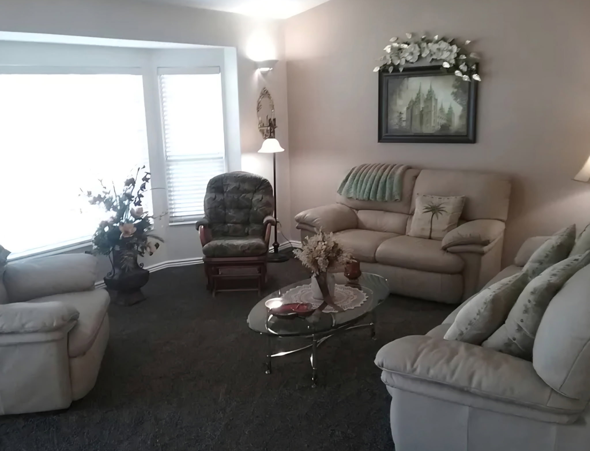 Living area featuring a bay window with blinds, neutral wall paint, and dark carpet flooring