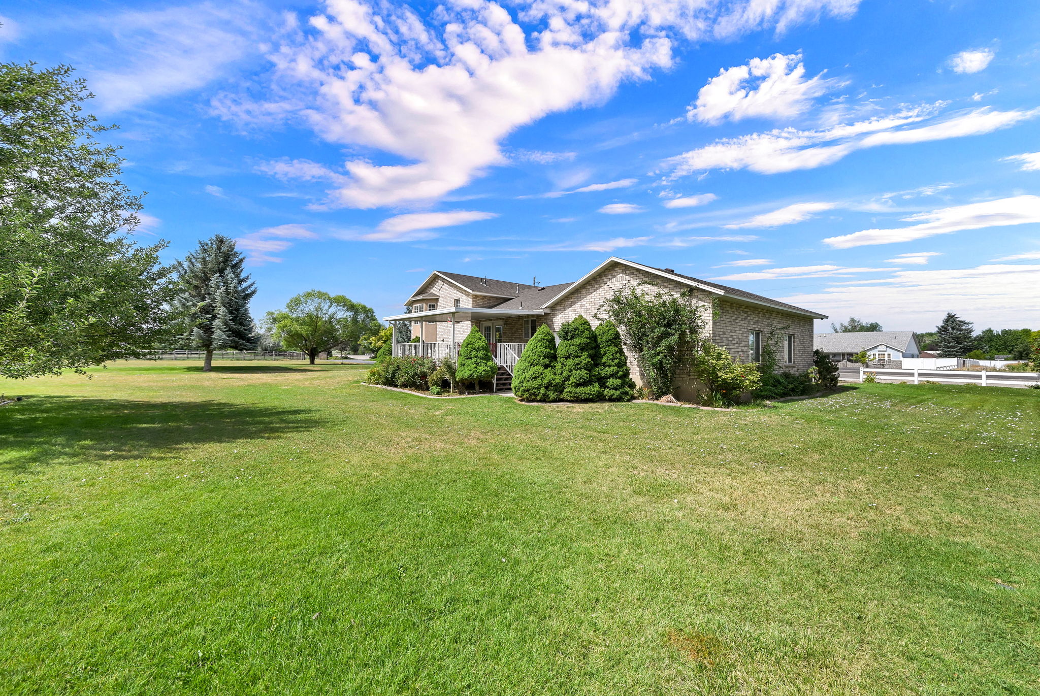 Expansive green lawn surrounds the property, featuring a multi-level structure with light brick siding and a dark shingle roof