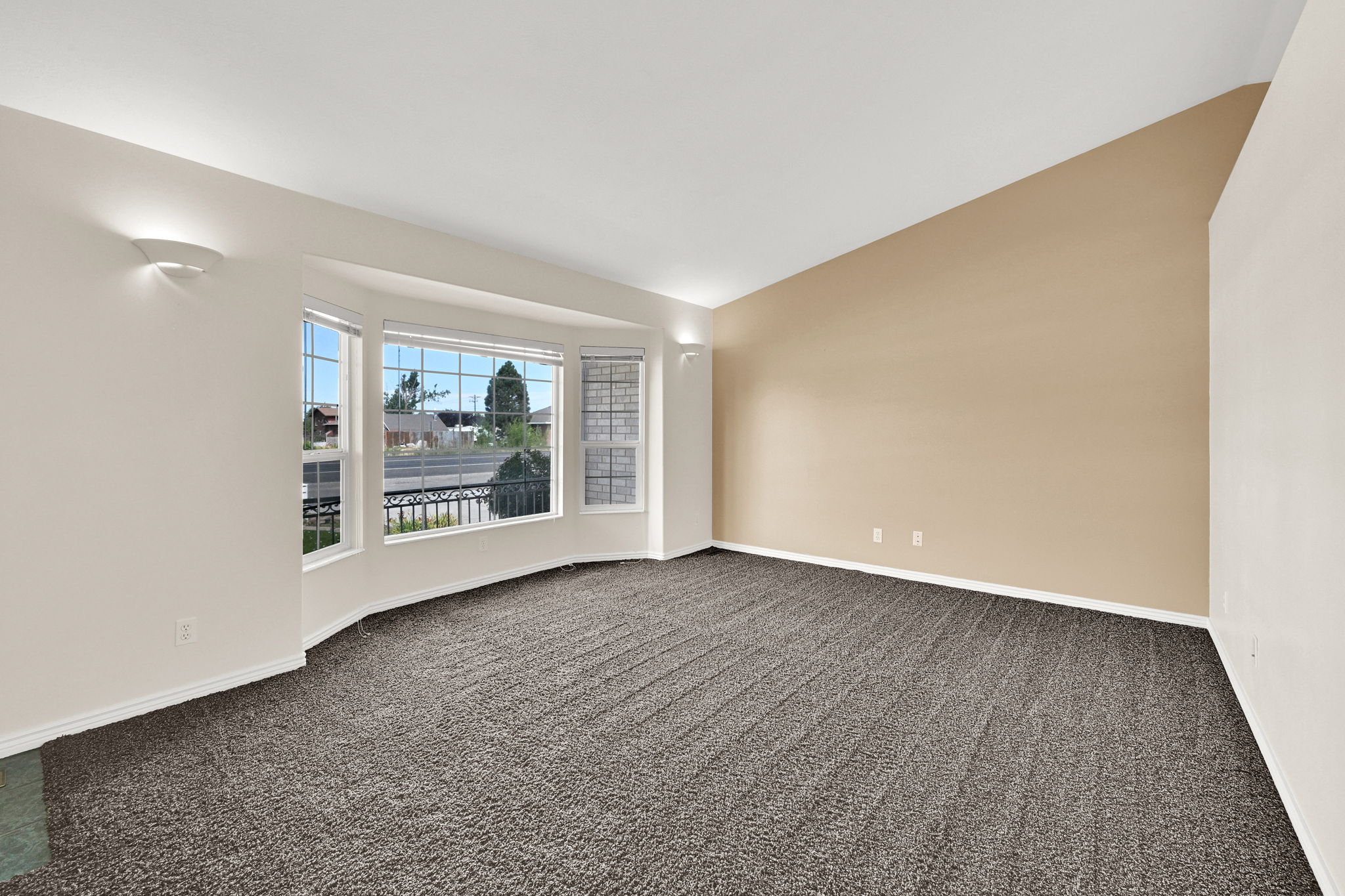 Spacious room featuring a bay window, wall-mounted sconce lighting, vaulted ceiling, and neutral-tone carpeting