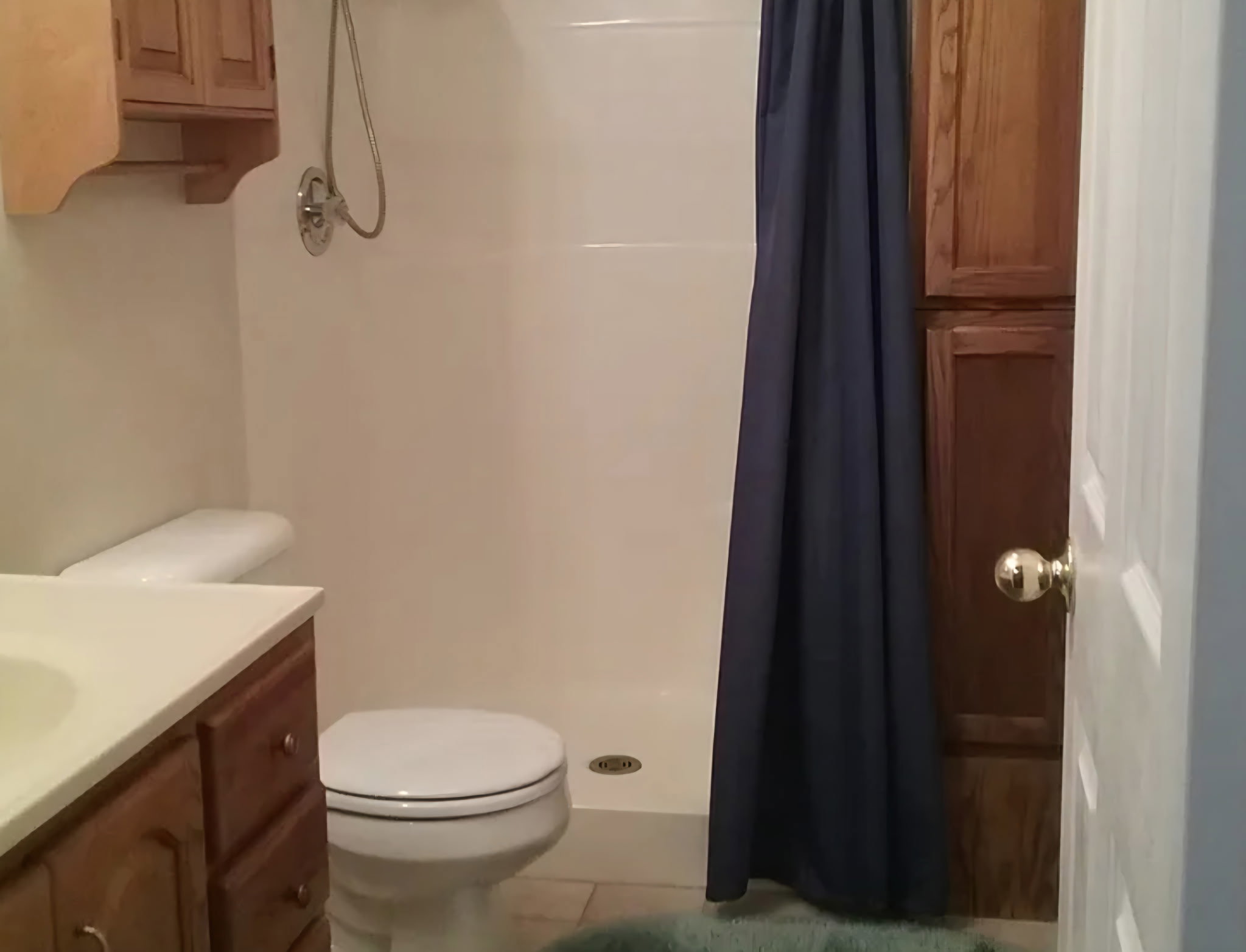 Bathroom featuring a white vanity with an integrated sink, a built-in toilet, a shower with a handheld fixture, and wood-finish cabinetry