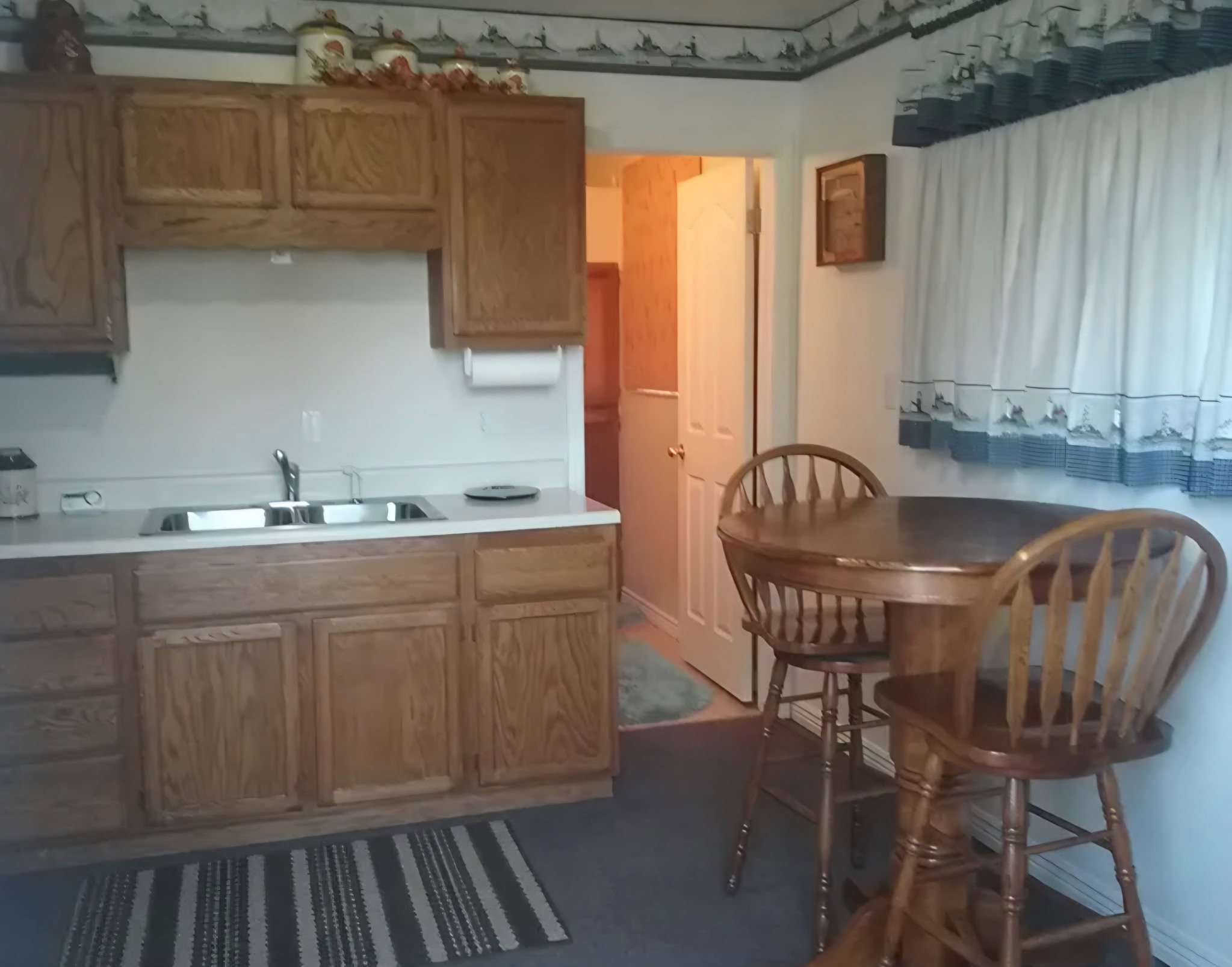 Kitchen area featuring wood-finish cabinetry, a double basin stainless steel sink, and light-toned countertops