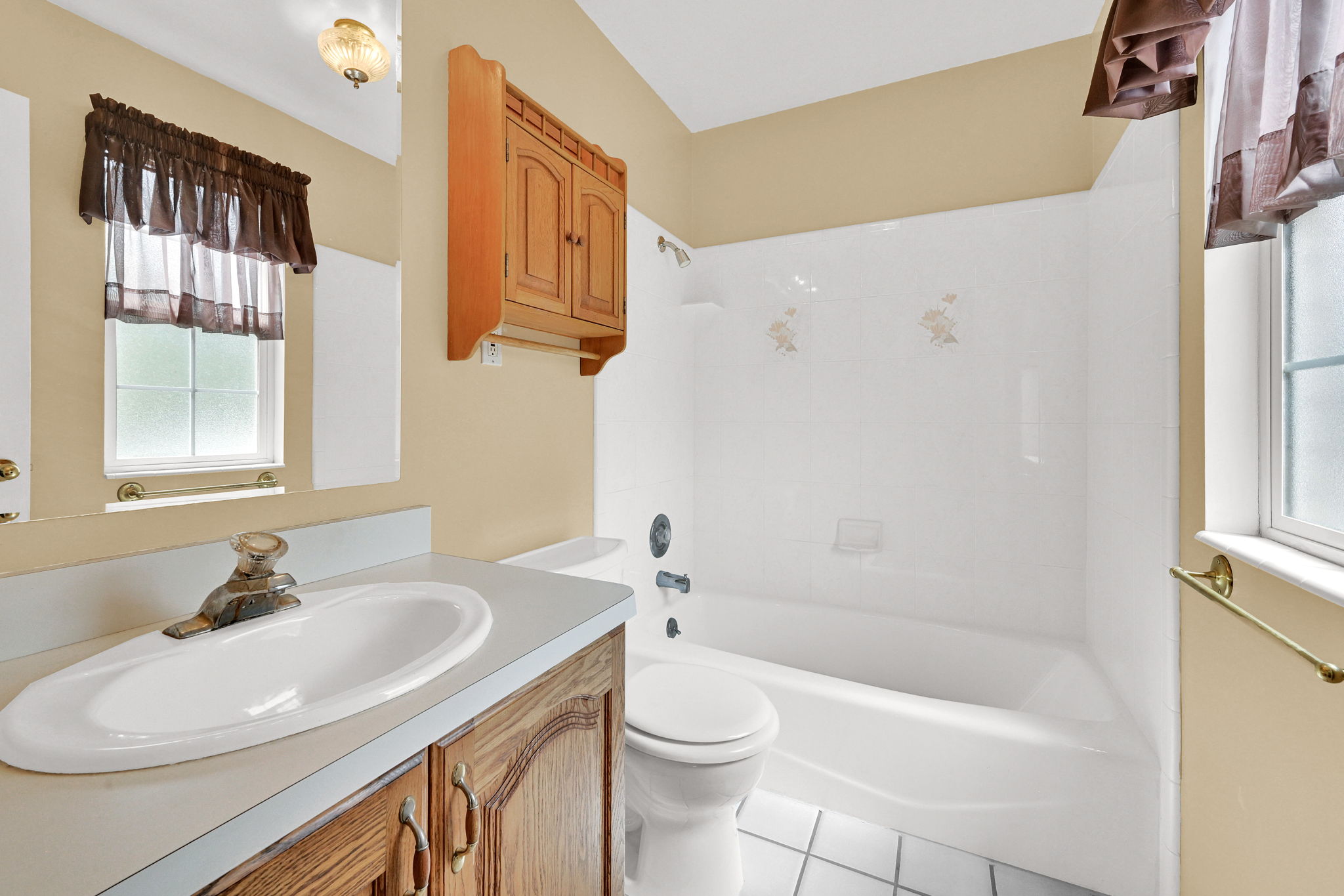 Bathroom featuring a wood-finish vanity with a white countertop, an oval sink, and a two-handle faucet