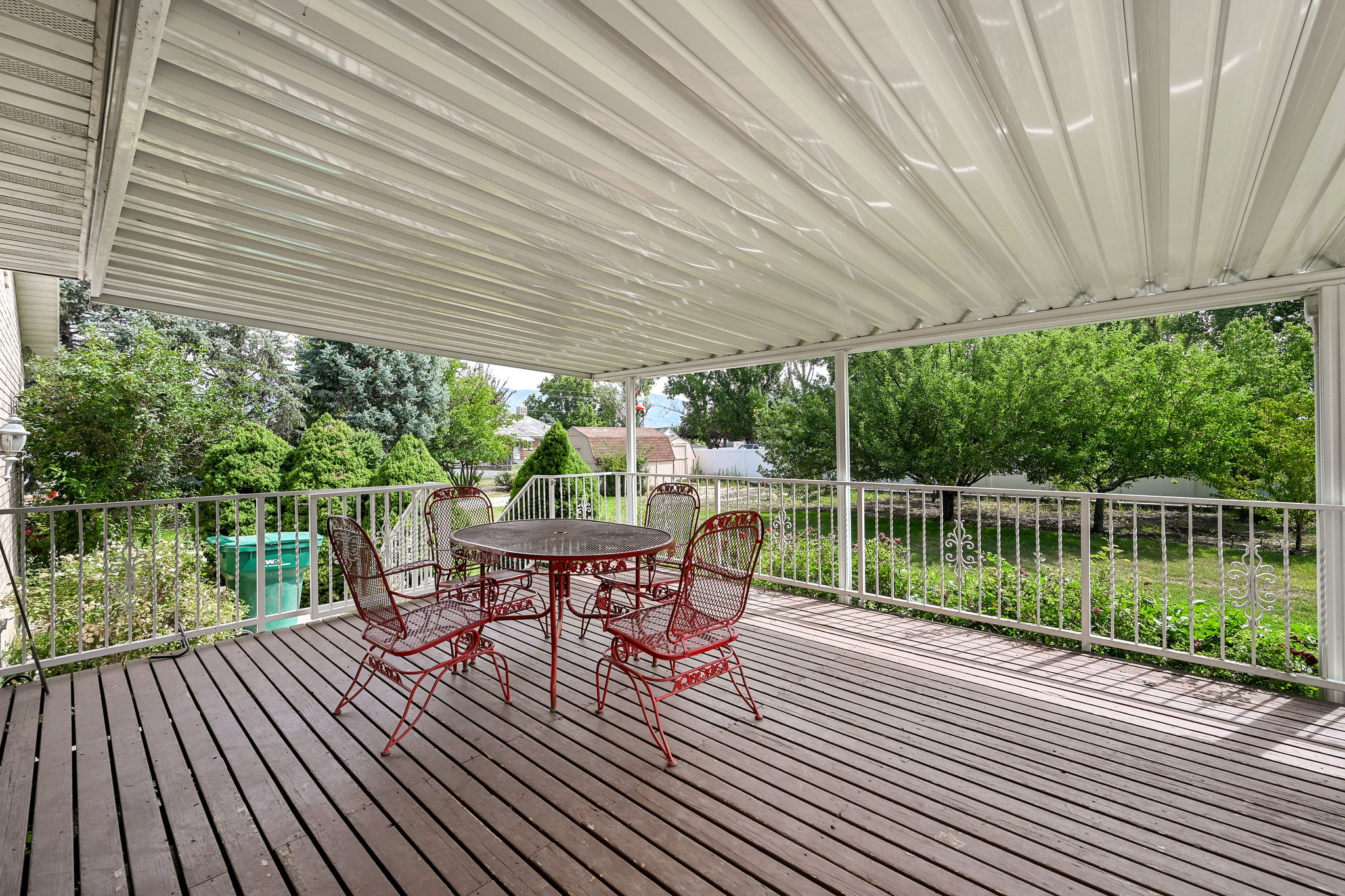 Spacious covered deck featuring wood-finish flooring, a white metal railing, and a corrugated metal ceiling