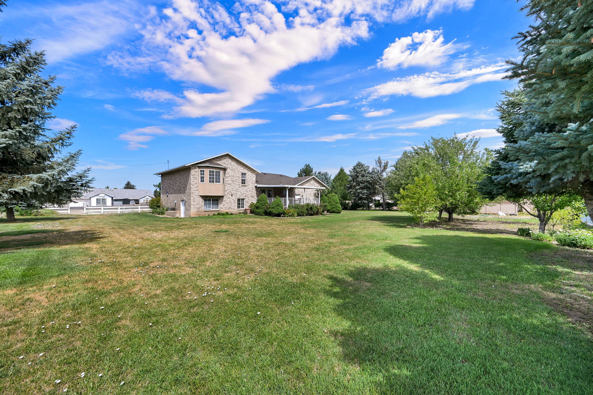 Spacious green lawn with mature trees and a stone-clad home featuring a covered porch