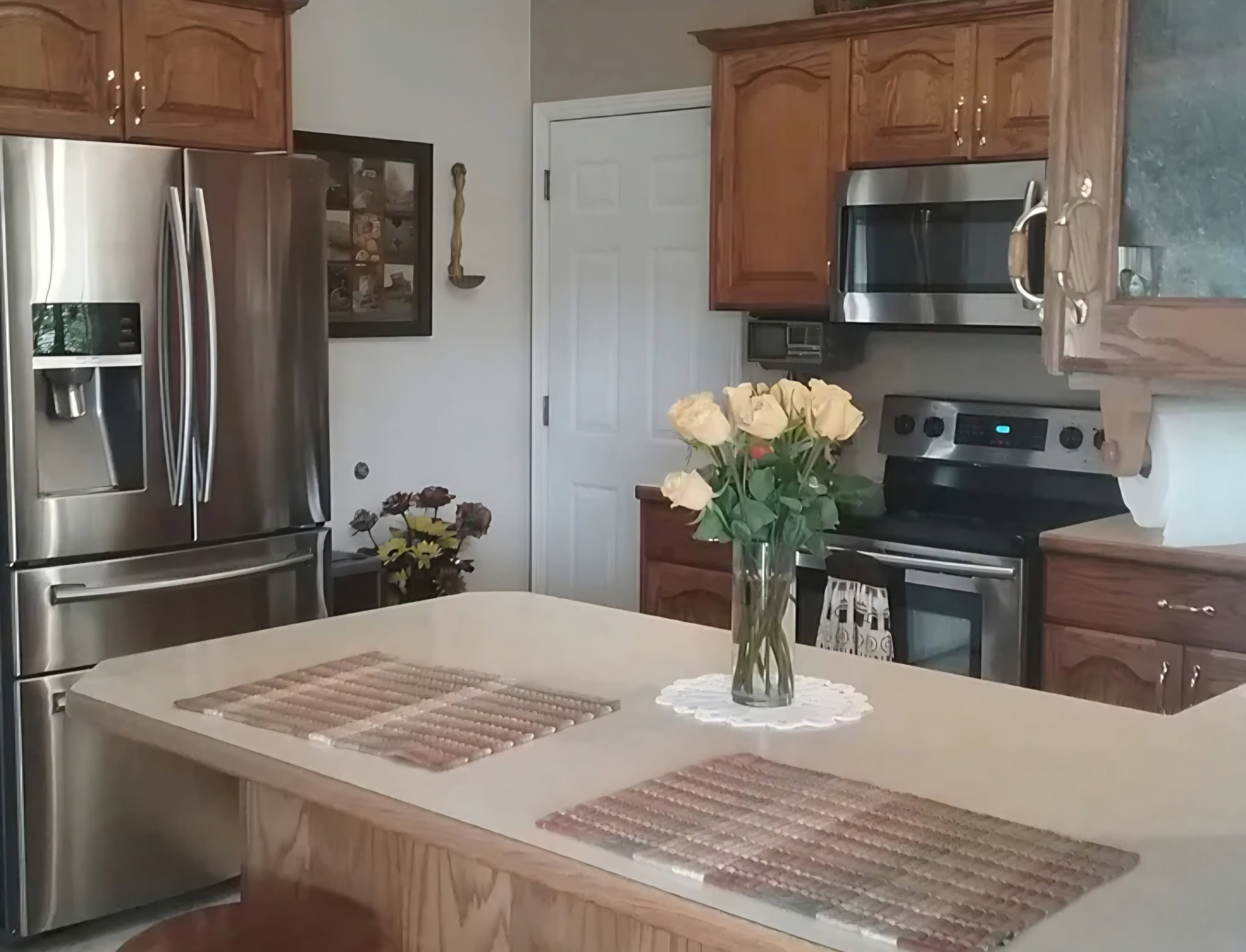 Kitchen featuring wood cabinetry, stainless steel appliances, a white paneled door, and a light-colored countertop island