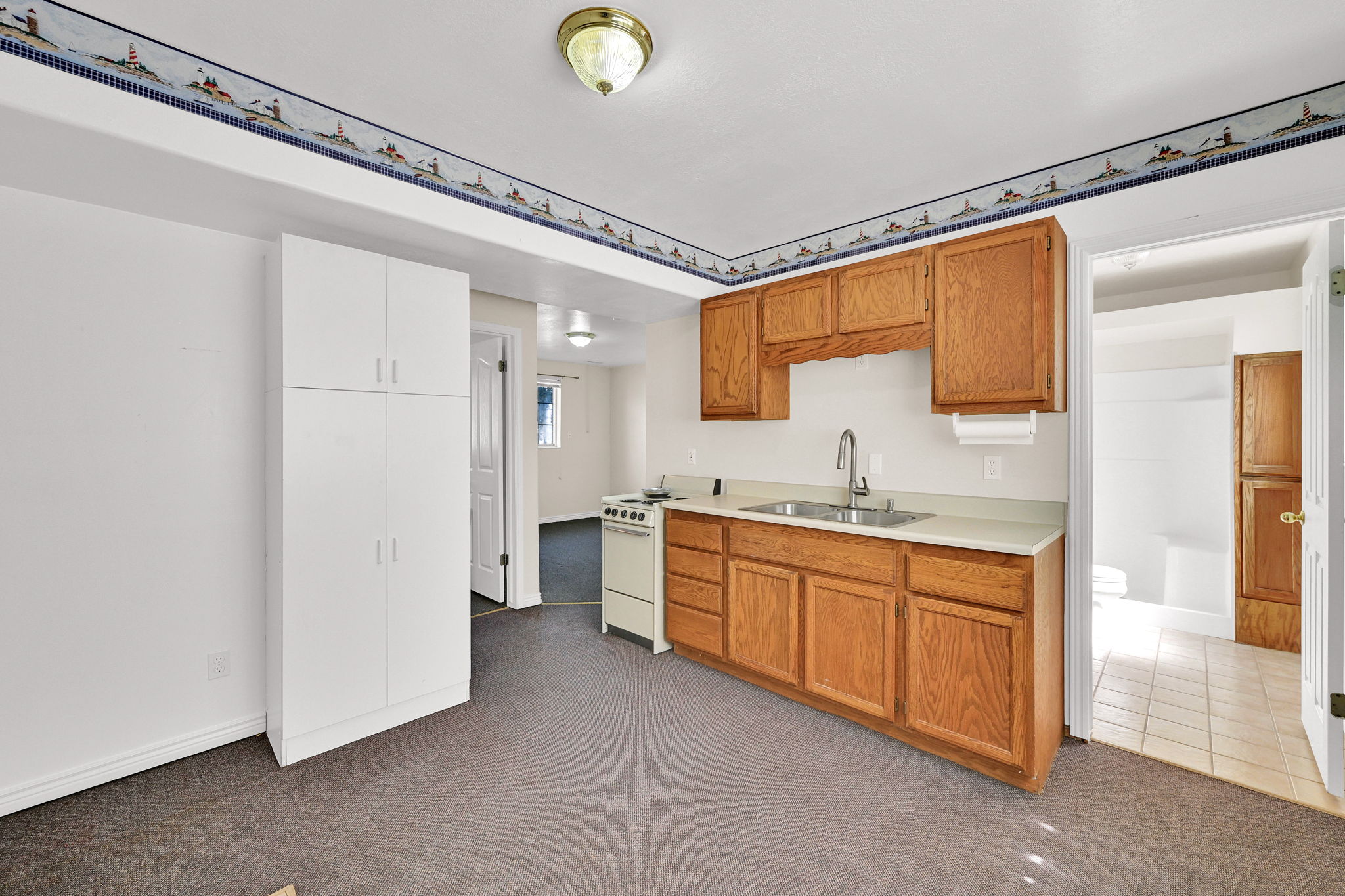 Kitchenette with wood cabinetry, light countertops, and a stainless steel sink