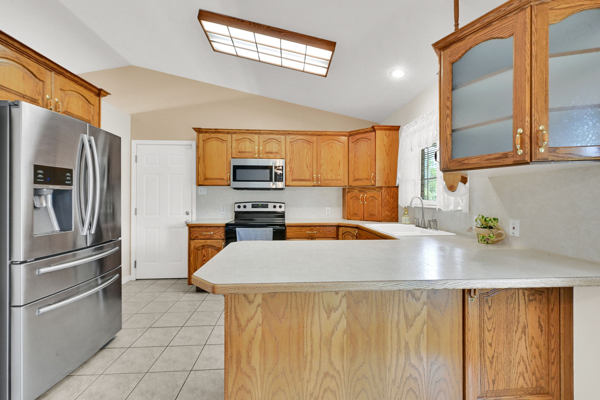 Kitchen featuring wood cabinetry, white countertops, stainless steel appliances, tiled flooring, and a vaulted ceiling with a skylight