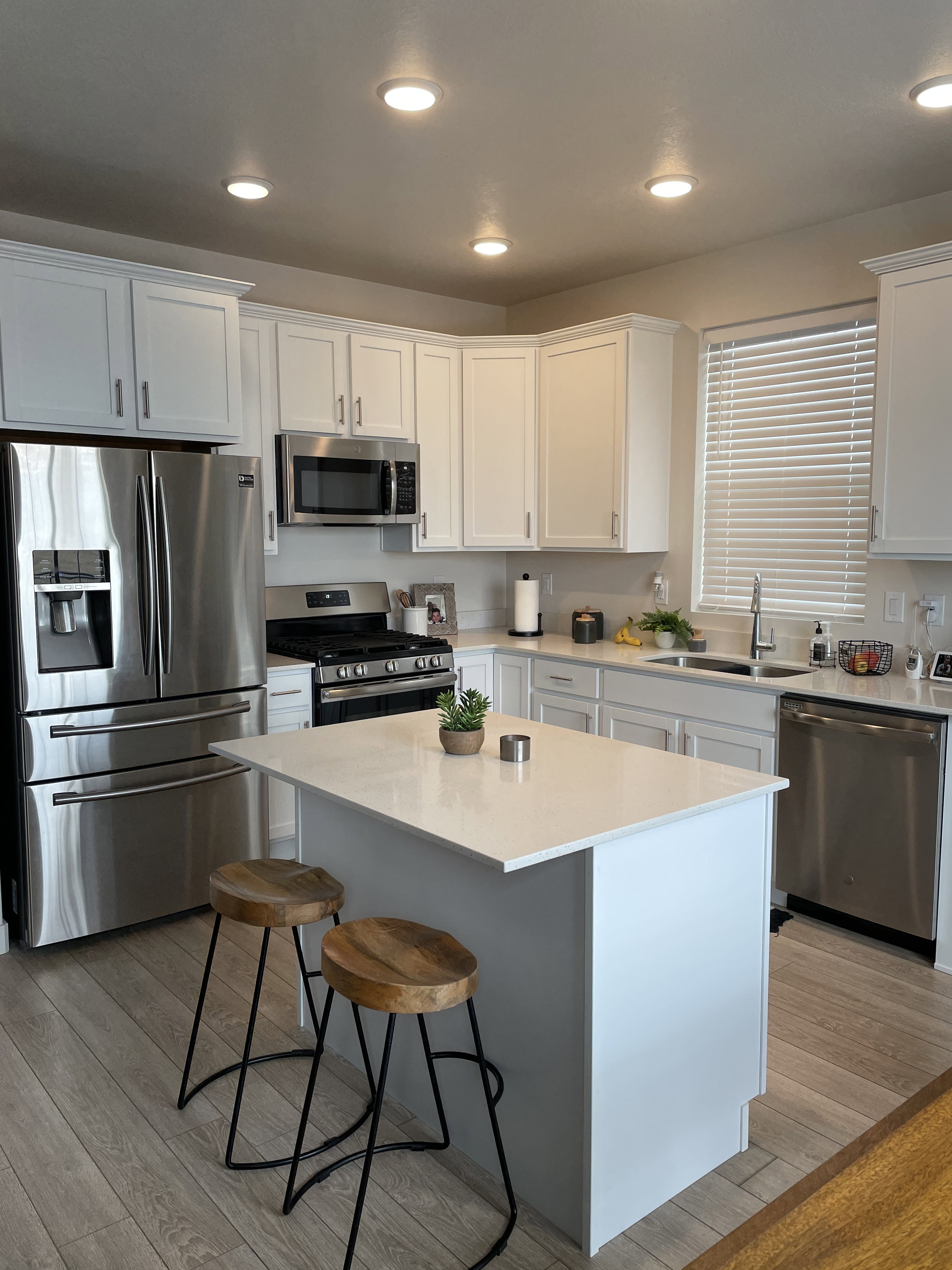 U-shaped kitchen featuring white cabinetry, stainless steel appliances, a center island with a light-toned countertop, wood-finish flooring, and recessed lighting