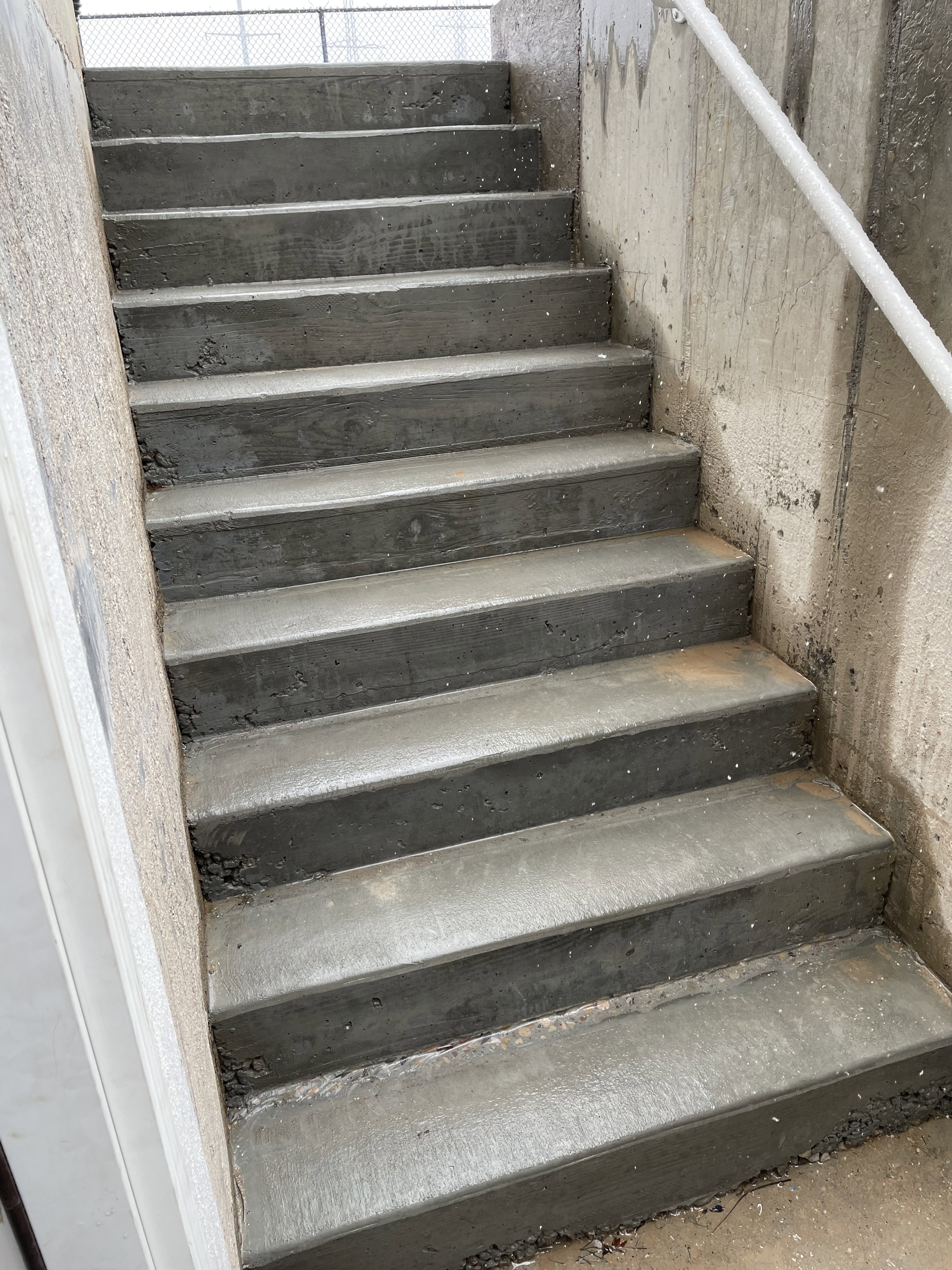 Concrete staircase with a white metal handrail and textured concrete wall