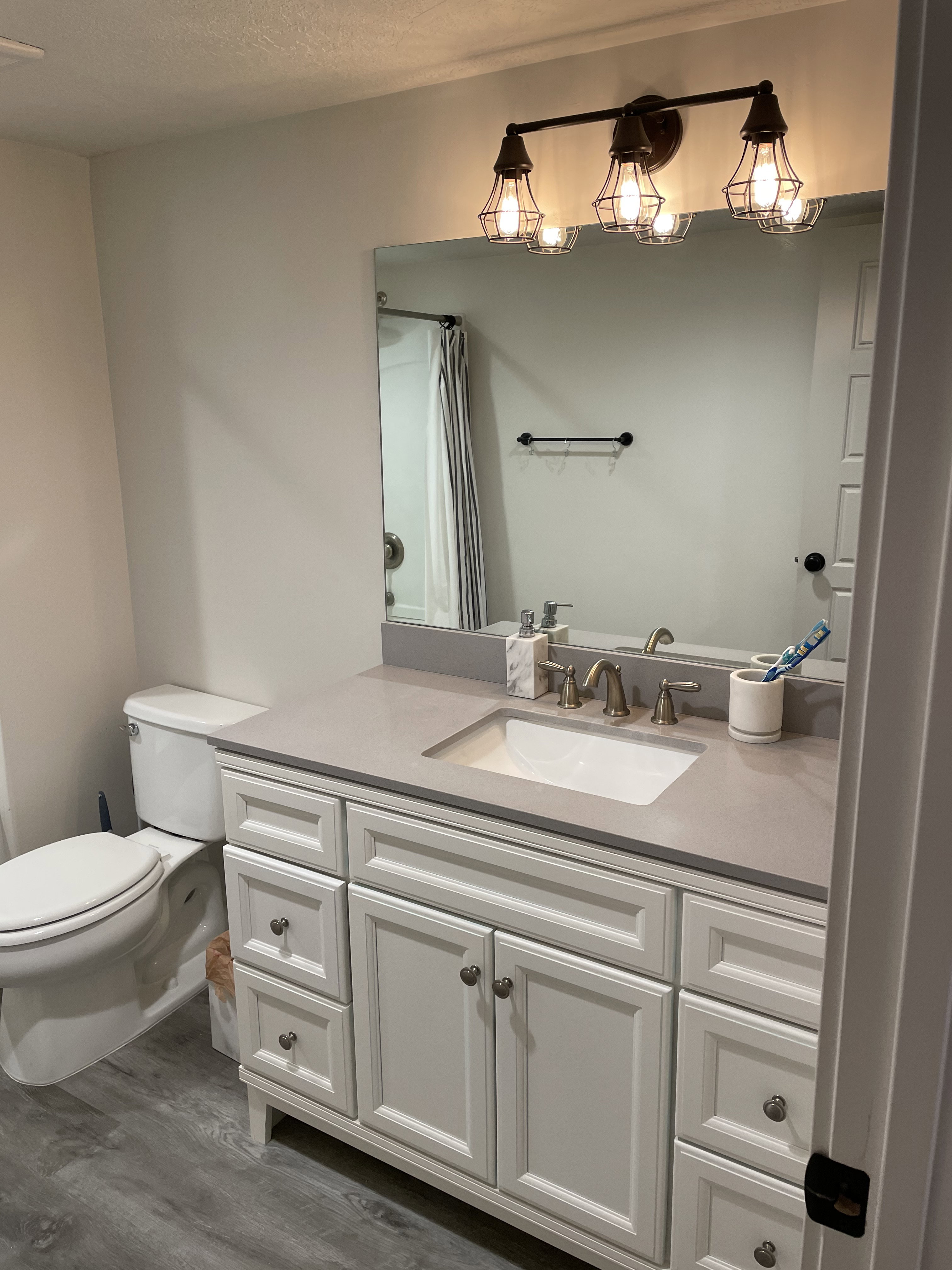 Bathroom vanity with a light gray countertop, white cabinetry, integrated sink, and an industrial-style bronze light fixture