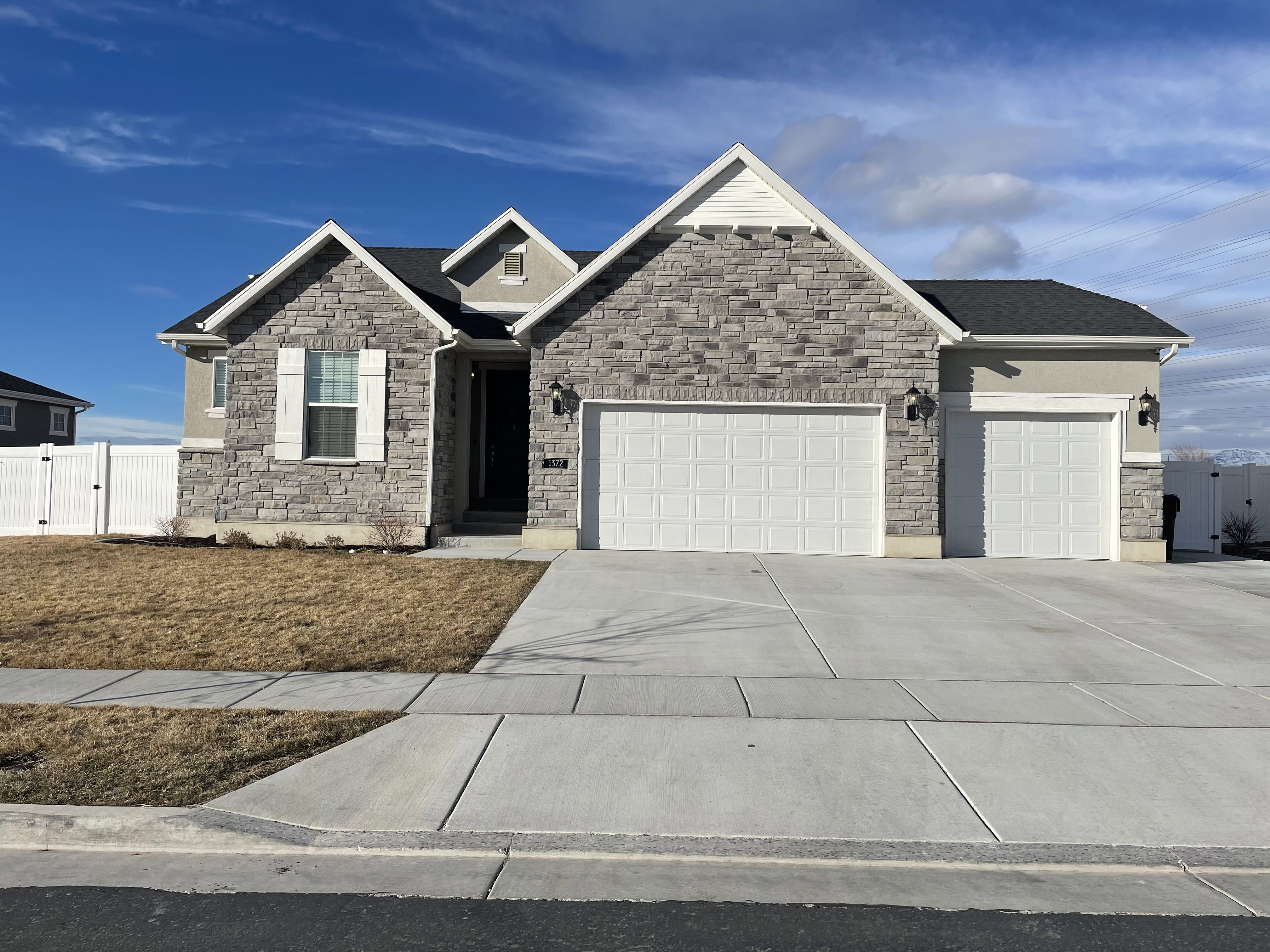 Stone and stucco exterior featuring a two-car garage, an additional single-car garage, and white vinyl fencing