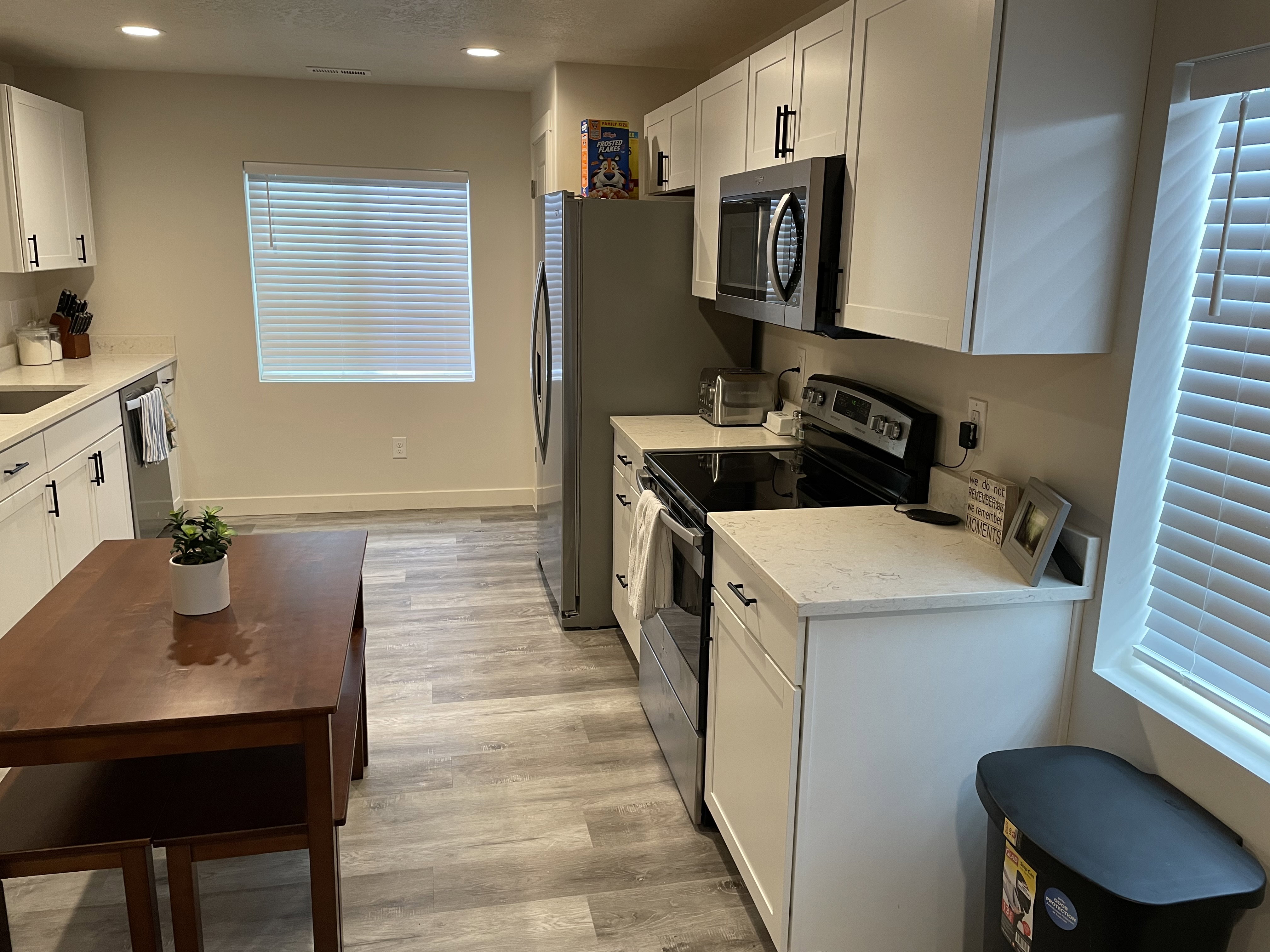 Contemporary kitchen featuring white cabinetry with black hardware, stainless steel appliances, light-toned countertops, and wood-finish flooring