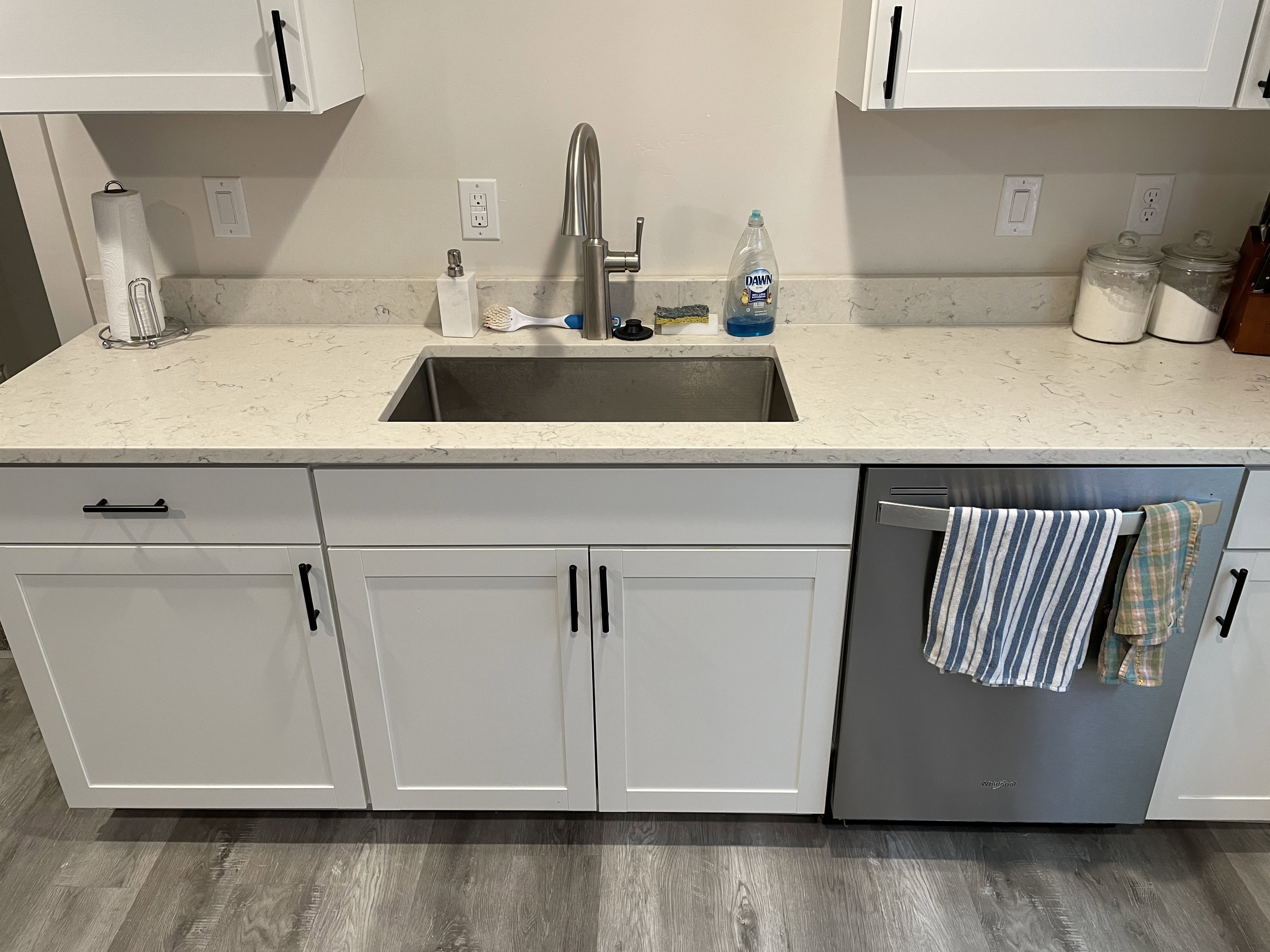Kitchen featuring light-toned countertops, a stainless steel sink, and white cabinetry with black hardware