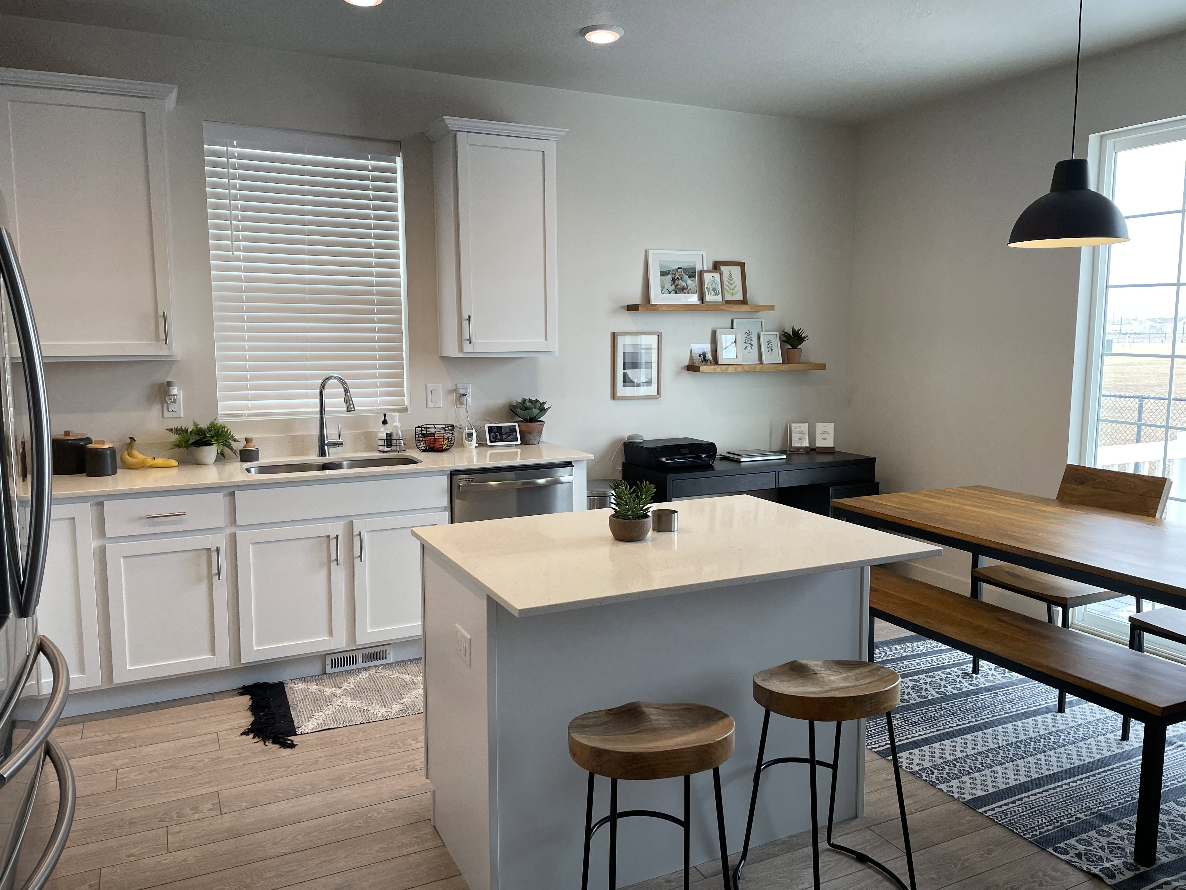Kitchen featuring a central island with countertop seating, light wood-finish flooring, white cabinetry, a stainless steel sink with a gooseneck faucet, and a large window with blinds