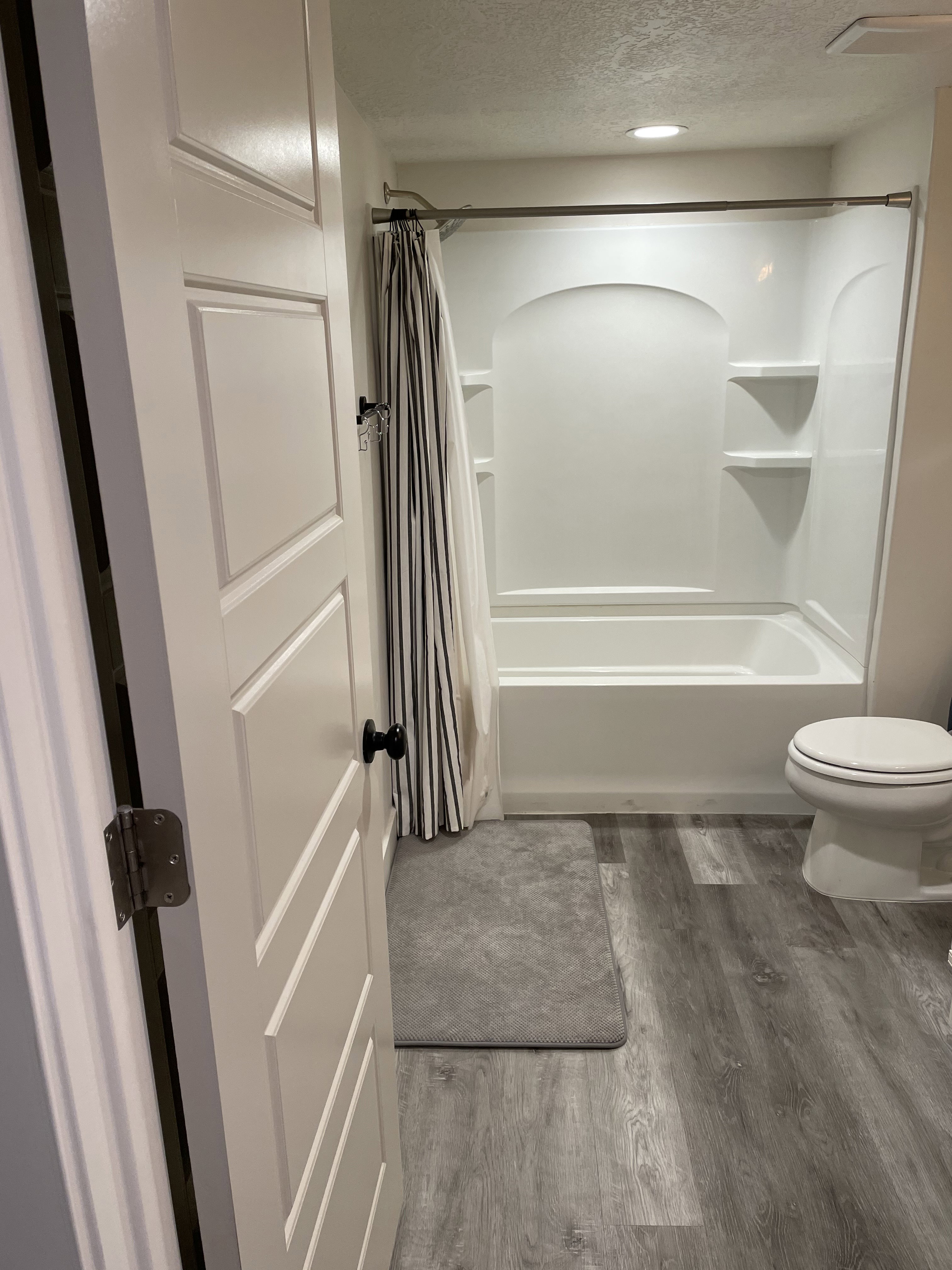 Bathroom featuring a white tub and shower combination with integrated shelving, a white toilet, and wood-finish flooring
