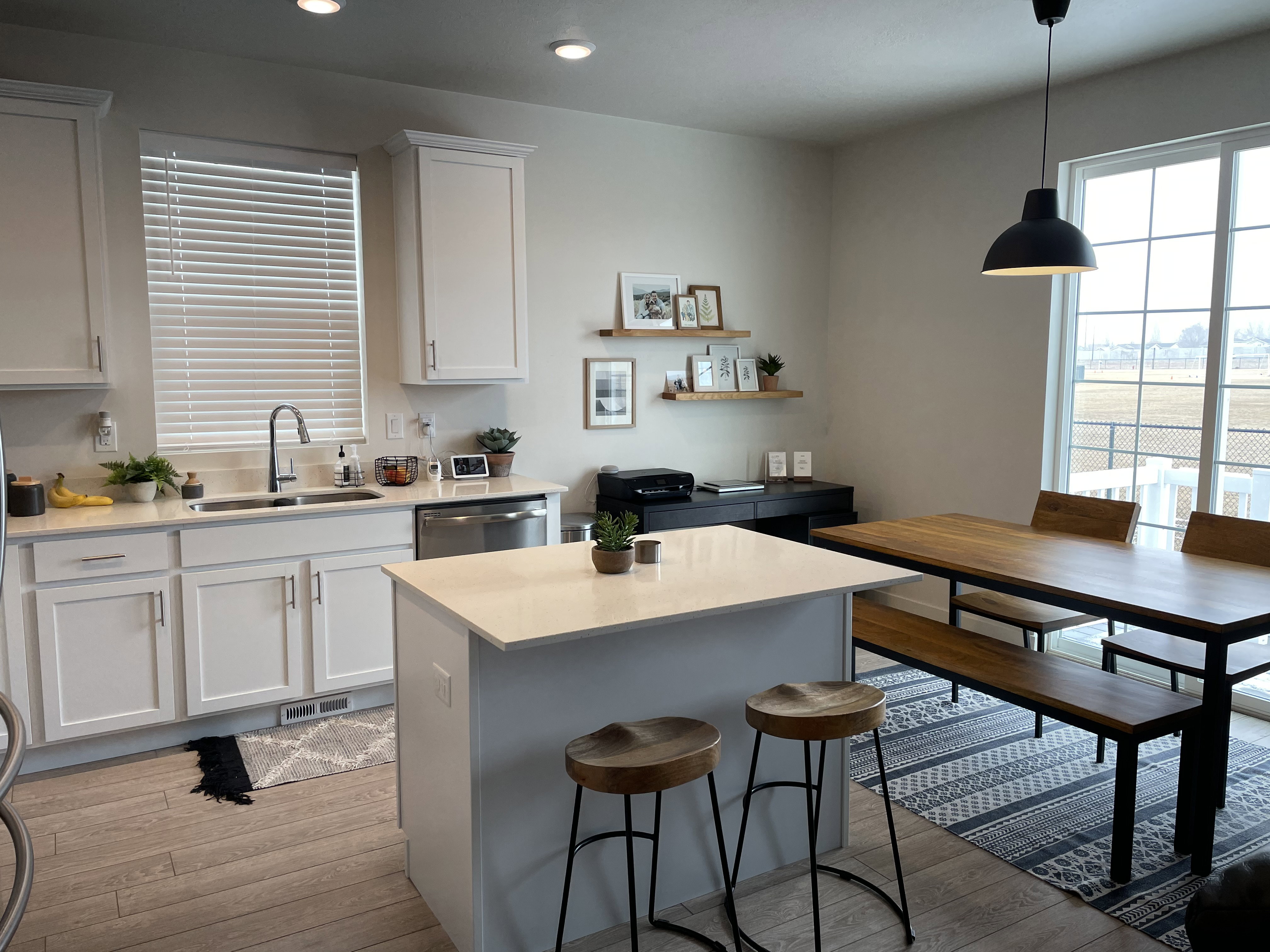 Modern kitchen and dining area featuring white shaker-style cabinetry, a central island with a light-toned countertop, wood-finish flooring, recessed lighting, and a sliding glass door providing outdoor access