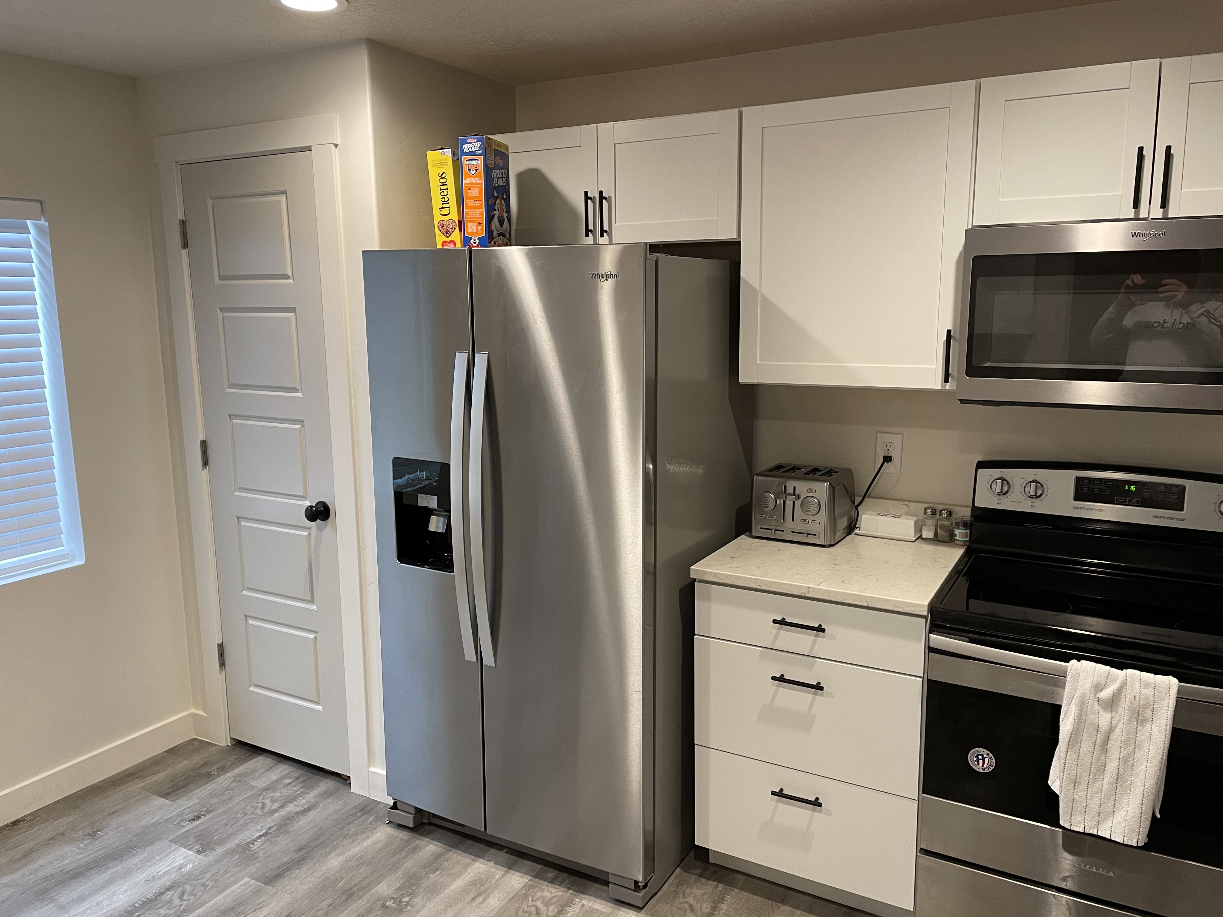 Contemporary kitchen featuring stainless steel appliances, white shaker-style cabinetry with matte black hardware, light-toned countertops, and wood-finish flooring