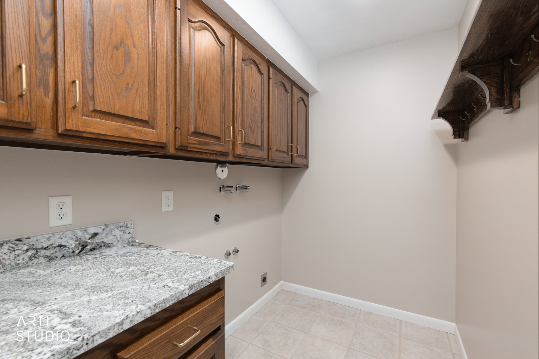 Laundry area featuring wood cabinetry with gold-tone hardware, a light-toned speckled countertop, and tiled flooring