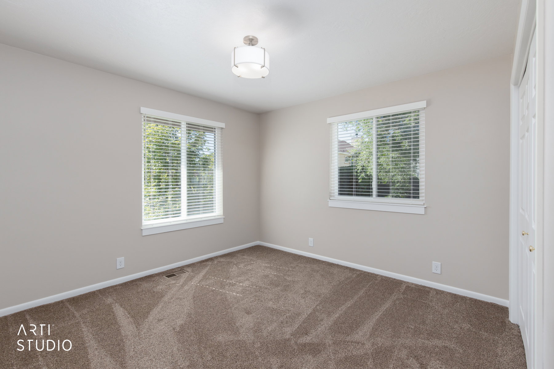 Carpeted room featuring two windows with white blinds, a semi-flush mount ceiling light, and light-toned walls