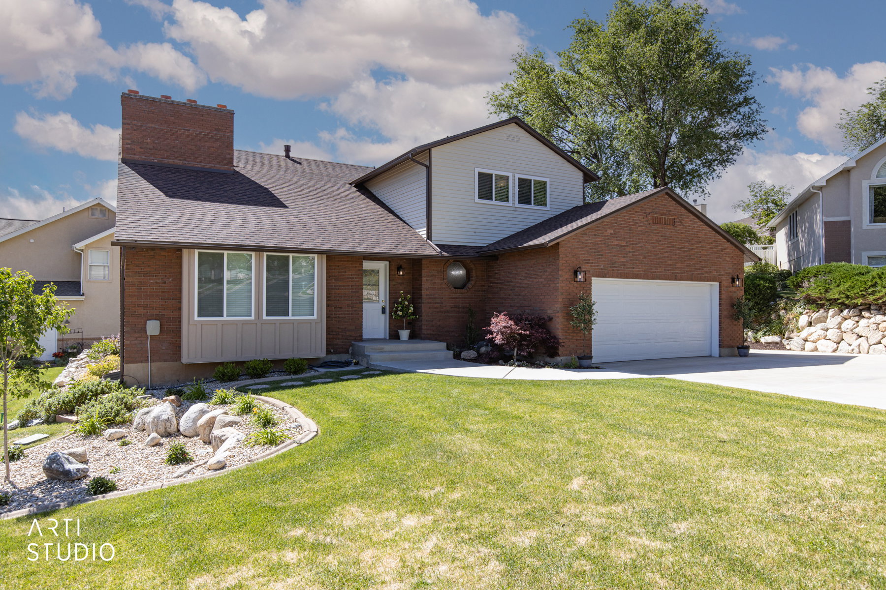 Brick and siding exterior featuring a prominent chimney, a two-car garage, and a concrete driveway