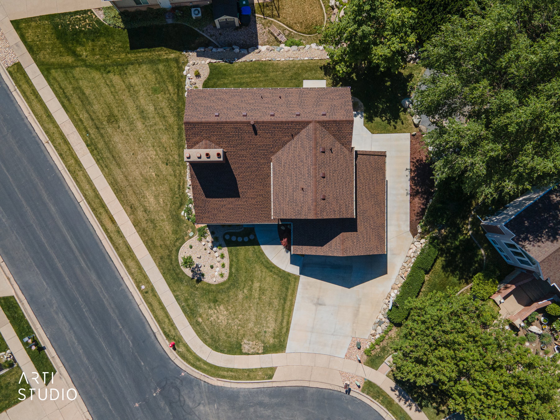 Overhead property perspective showcasing a brown shingle roof, concrete driveway, and established landscaping with mature trees