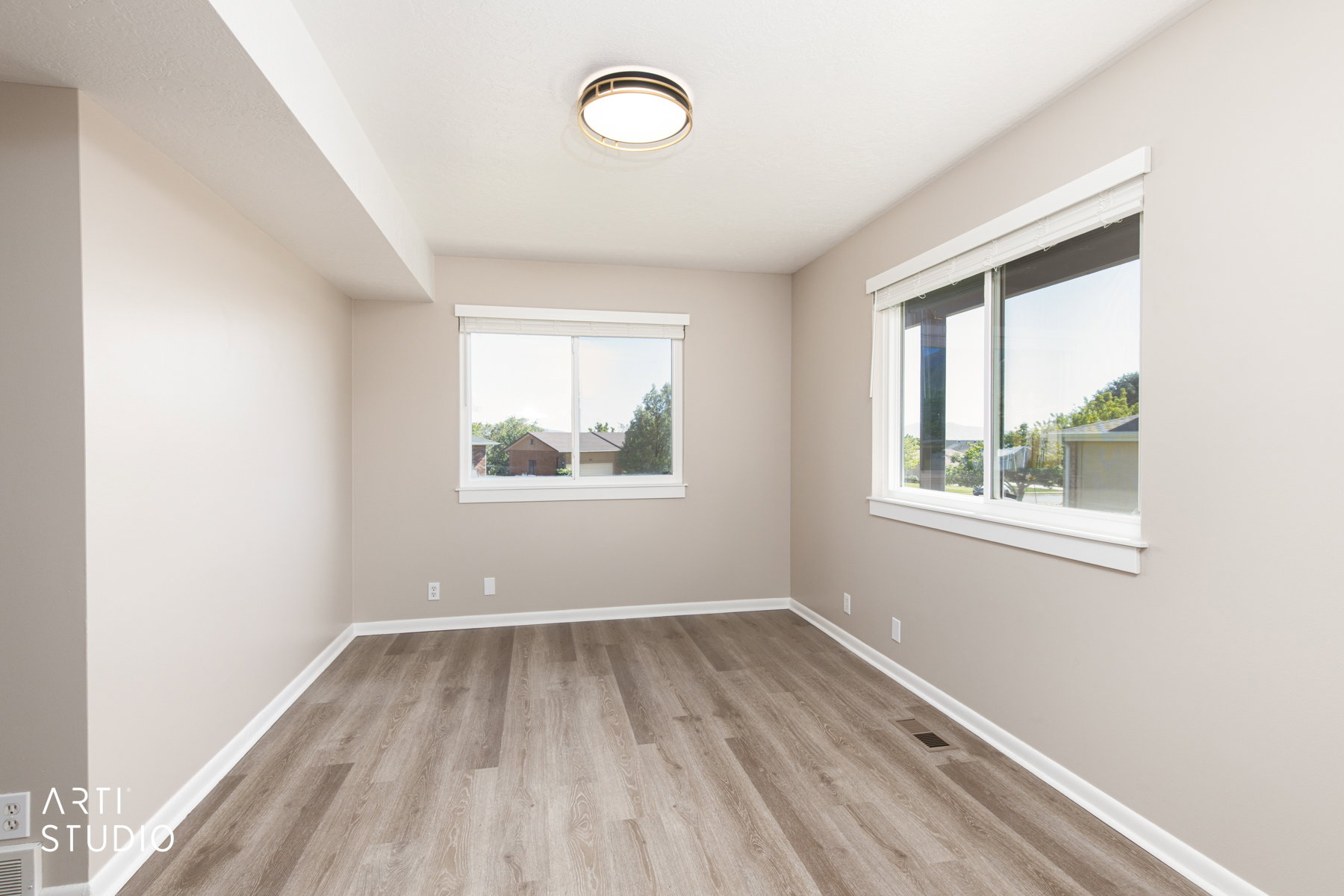 Spacious room featuring wood-finish flooring, two large windows with white trim, a flush-mount ceiling light fixture, and neutral painted walls