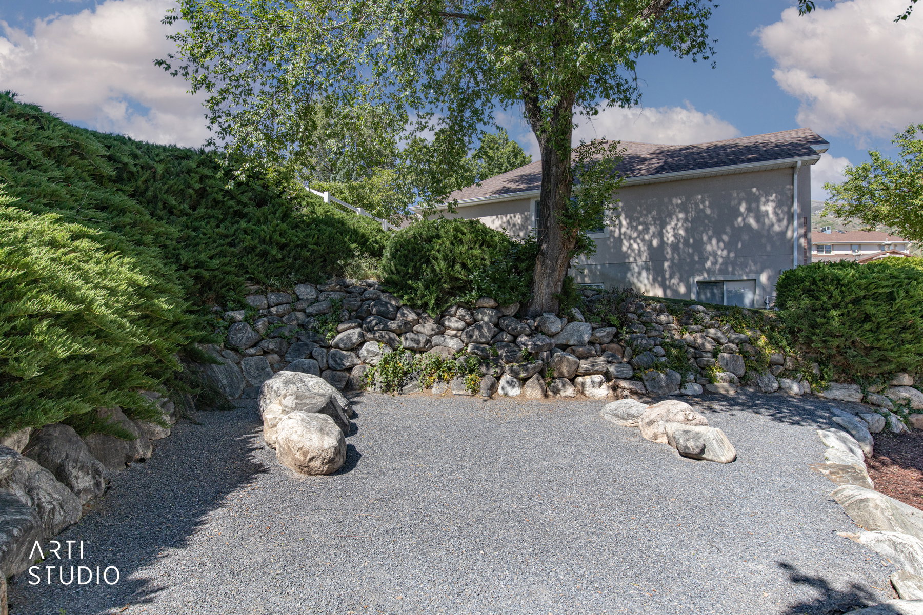 Landscaped outdoor area featuring a gravel surface, natural rock retaining walls, and established shrubbery