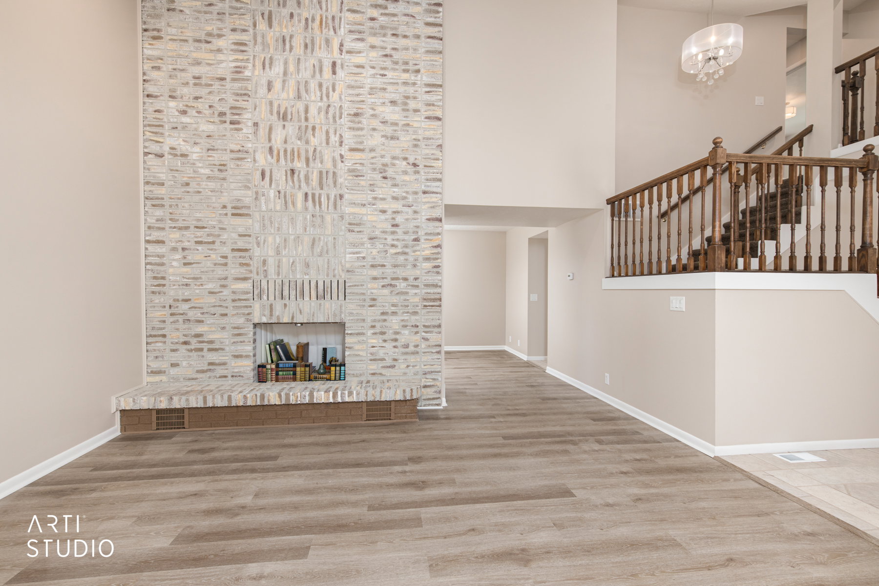 Great room featuring a full-height brick fireplace, wood-finish flooring, high ceilings, and an elegant chandelier
