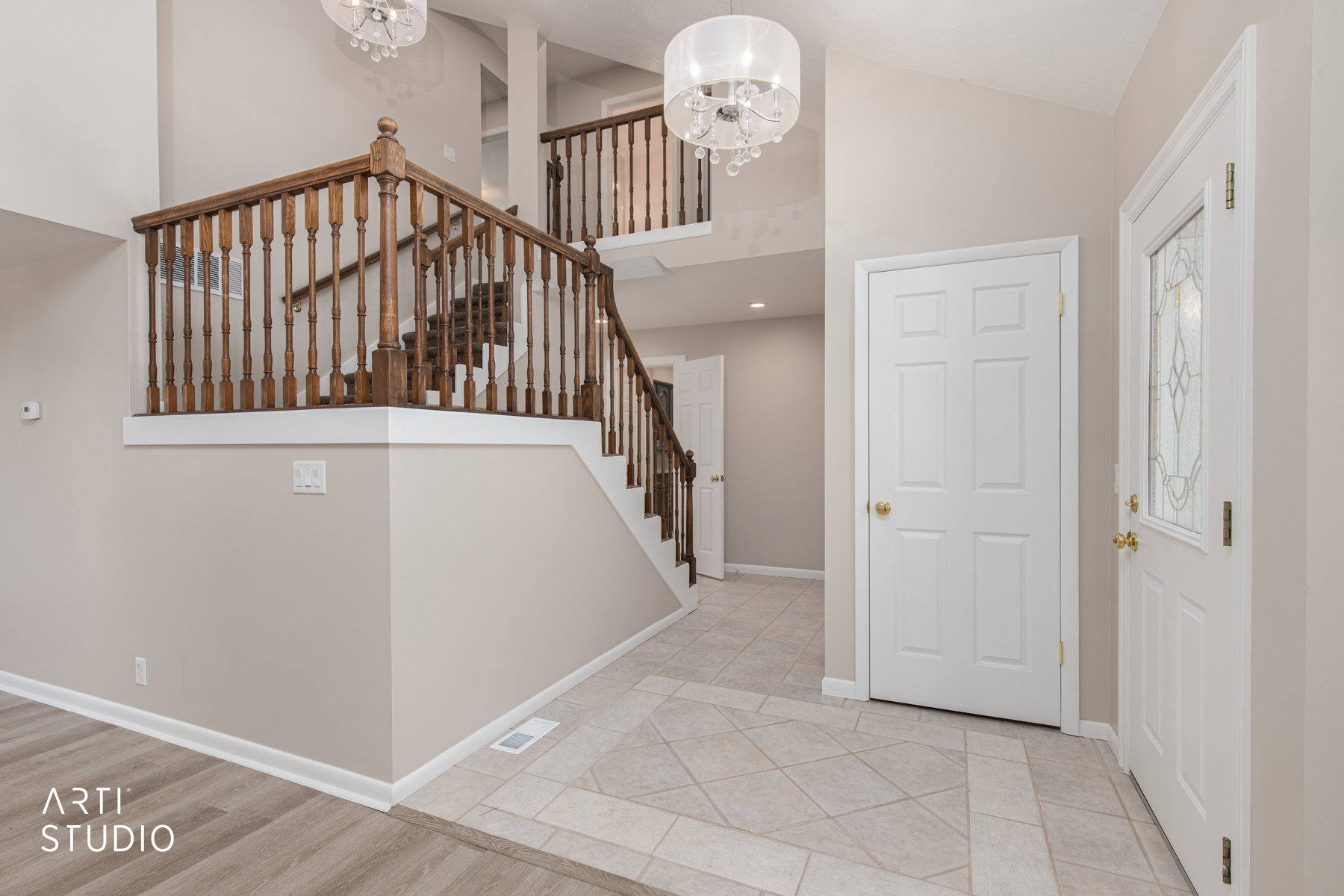 Two-story foyer featuring a grand staircase with wood banisters, decorative tile flooring, high ceilings, and two contemporary chandeliers