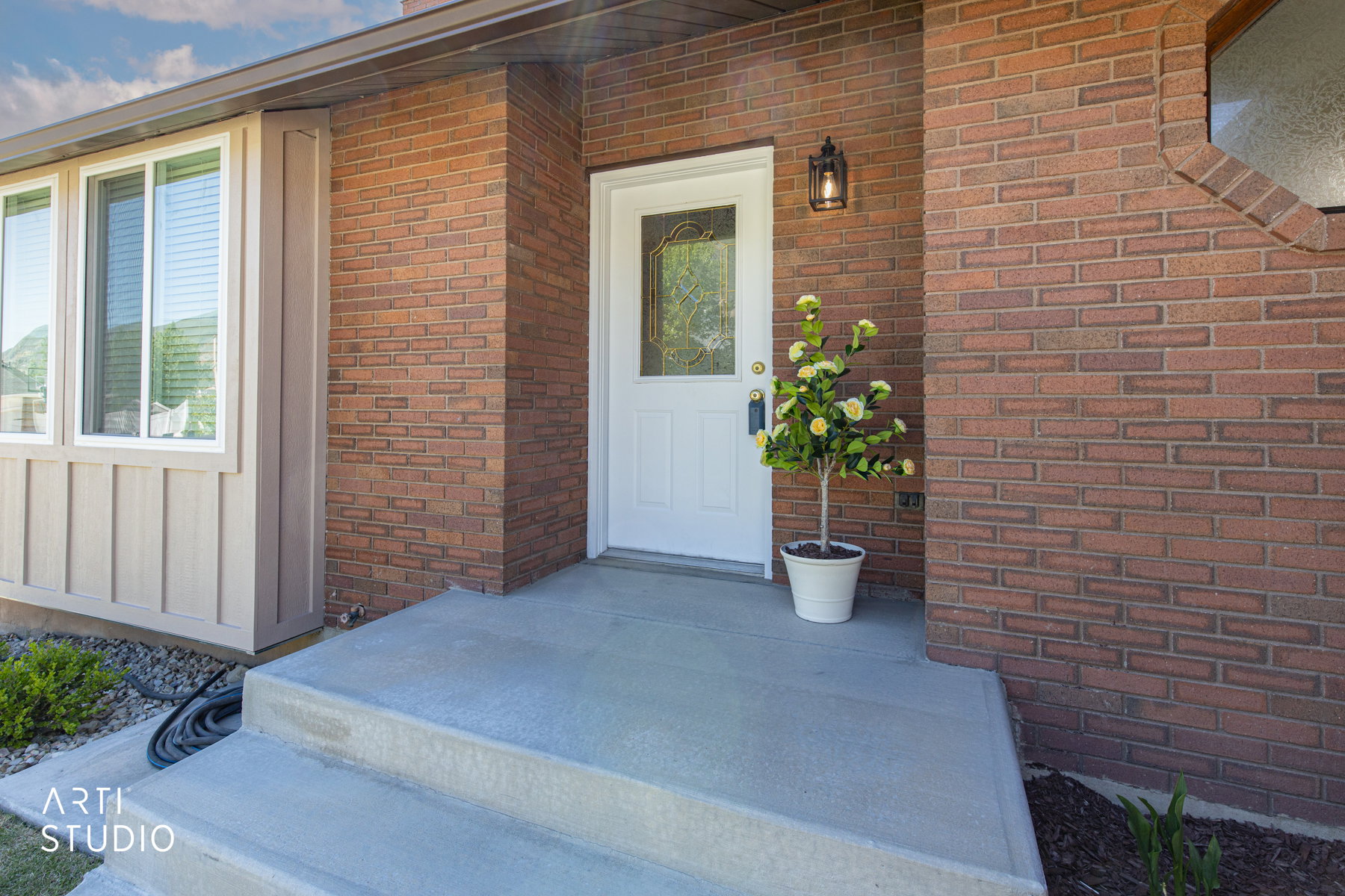 Brick exterior with a white entry door featuring decorative glass, a concrete front stoop, and an exterior wall lantern