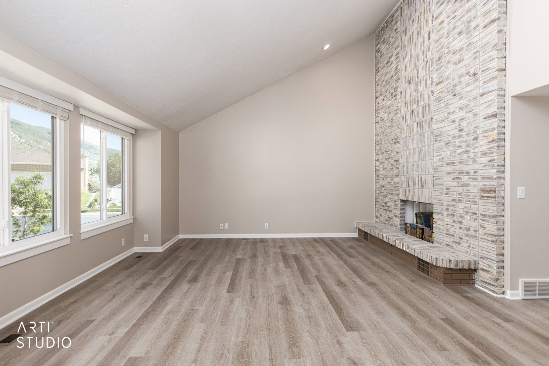 Spacious living area featuring a vaulted ceiling, wood-finish flooring, and a floor-to-ceiling brick fireplace