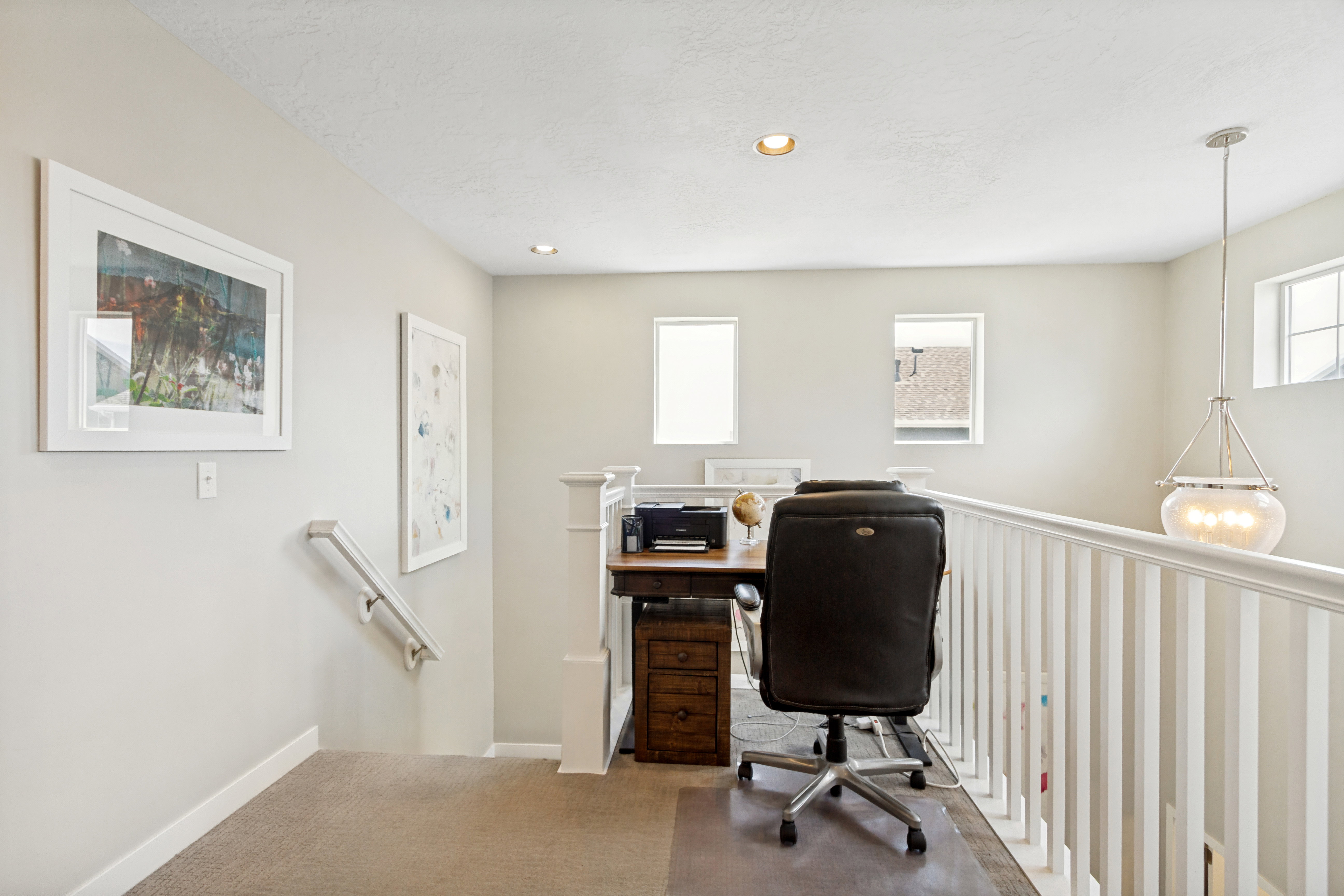 Open loft area featuring a built-in desk, white painted railing, recessed lighting, and a suspended glass pendant light