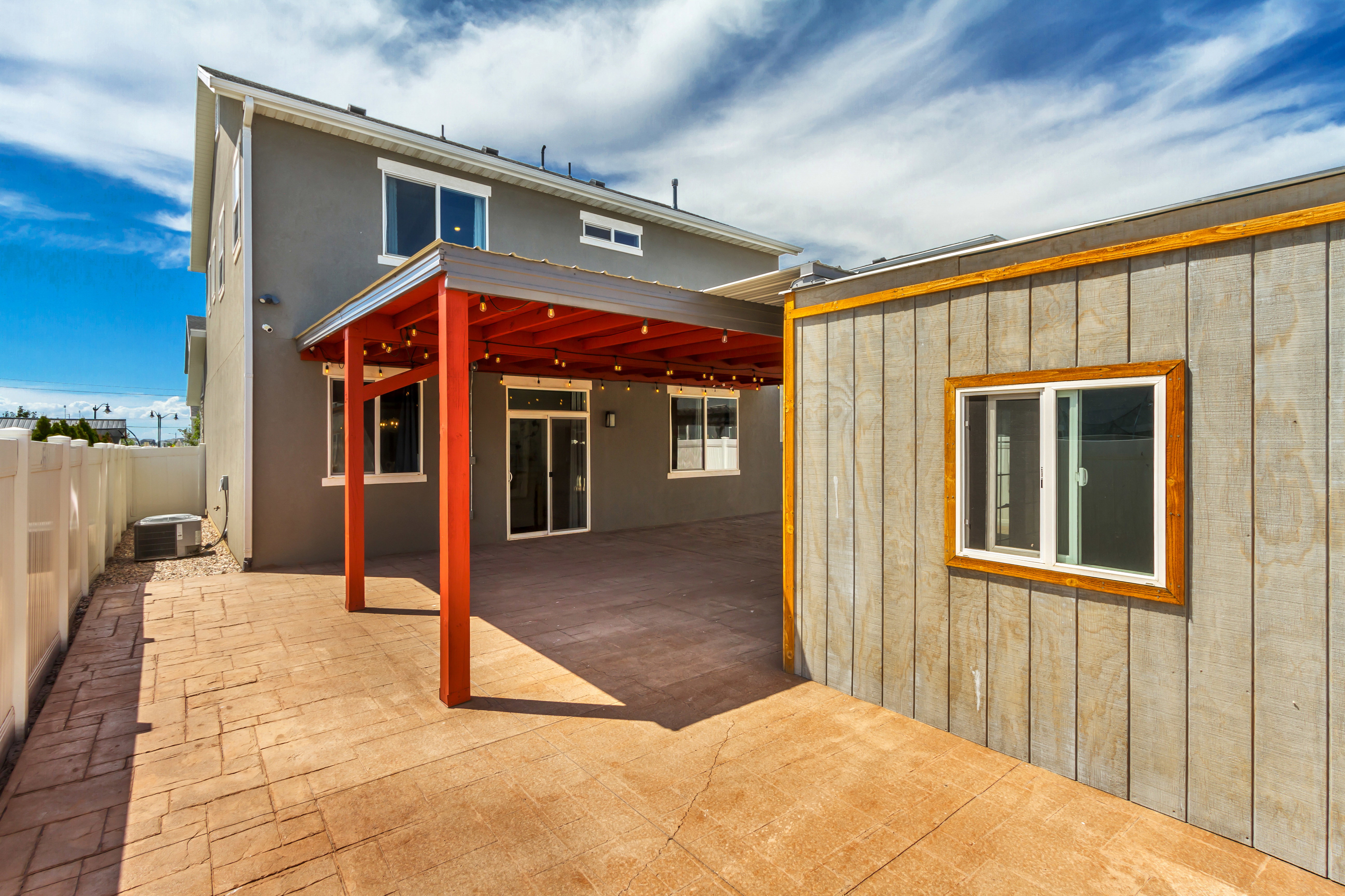 Expansive stamped concrete patio featuring a vibrant red pergola with string lighting