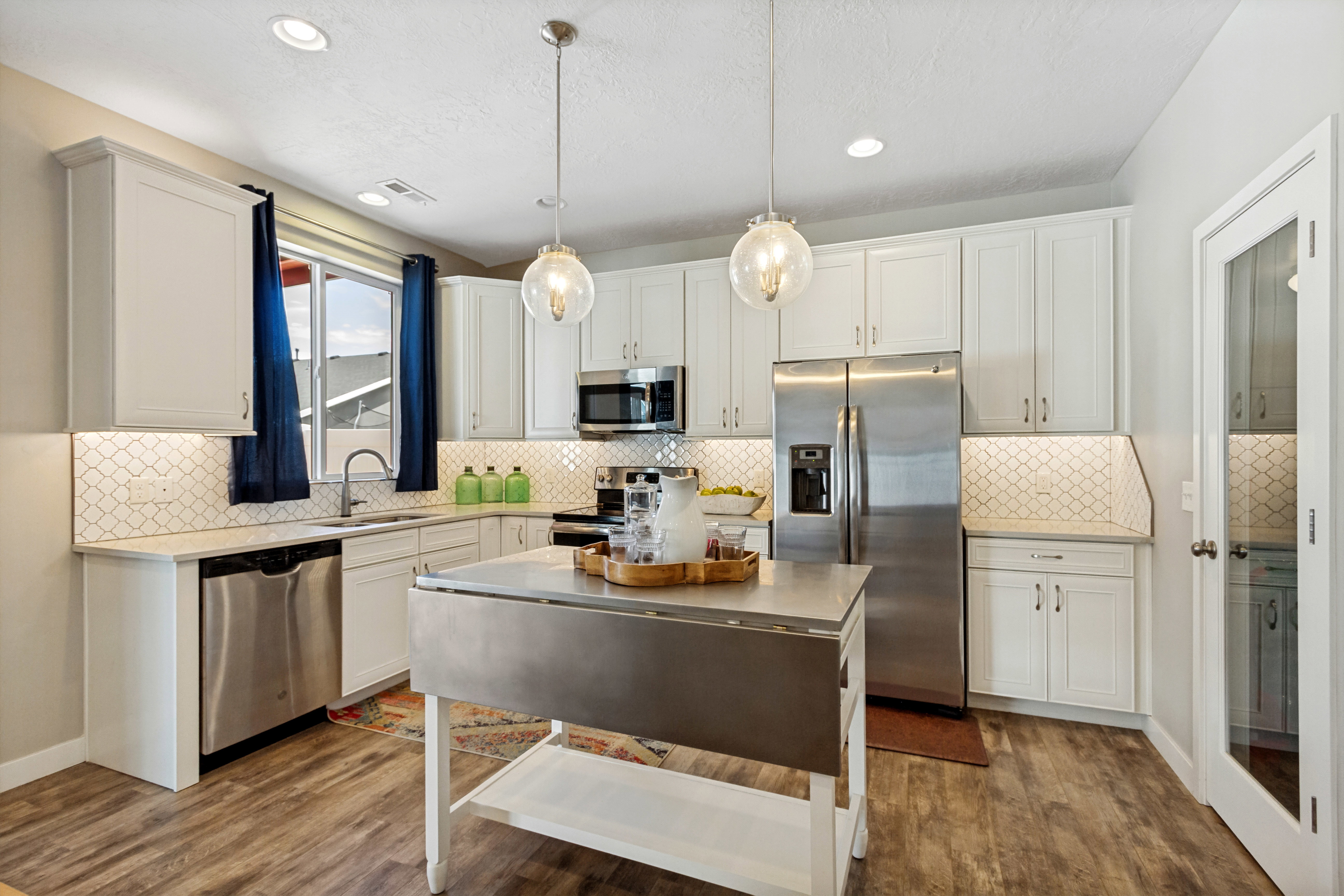 Contemporary kitchen featuring white cabinetry, stainless steel appliances, wood-finish flooring, recessed lighting, and a patterned tile backsplash