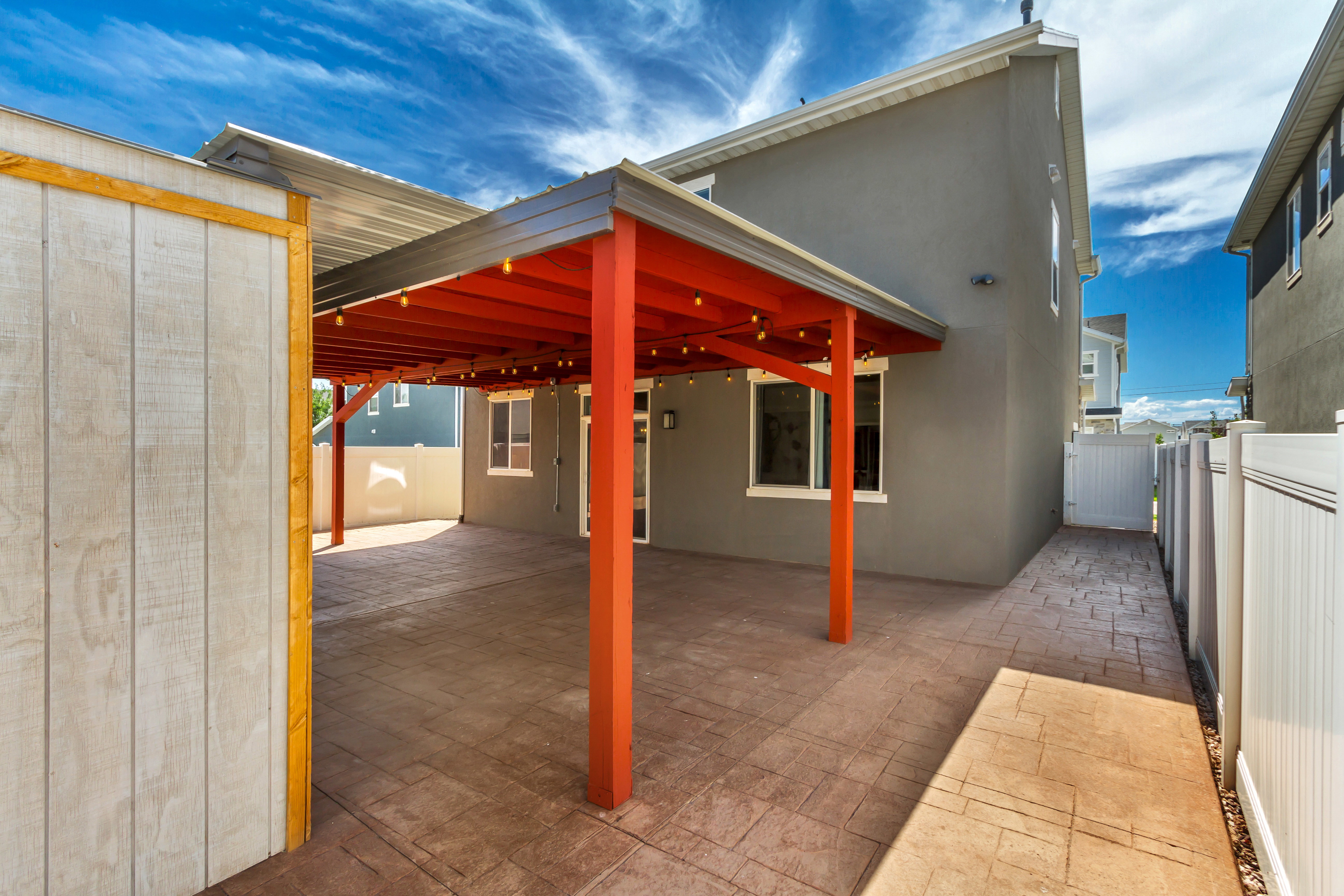 Covered patio with stamped concrete flooring, supported by orange-toned columns and ceiling beams