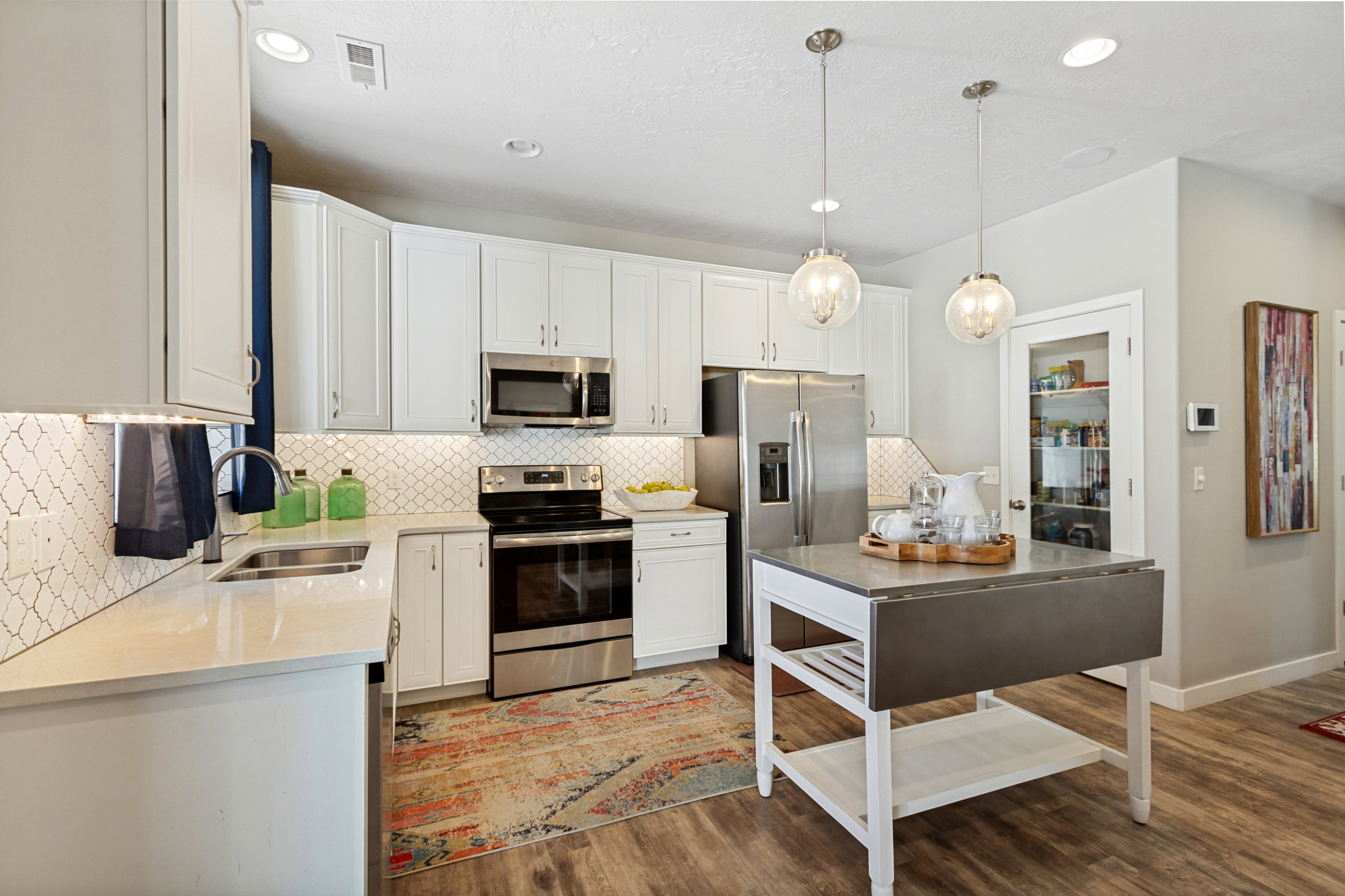 Modern kitchen featuring white cabinetry, stainless steel appliances, light countertops, a decorative tile backsplash, and wood-finish flooring