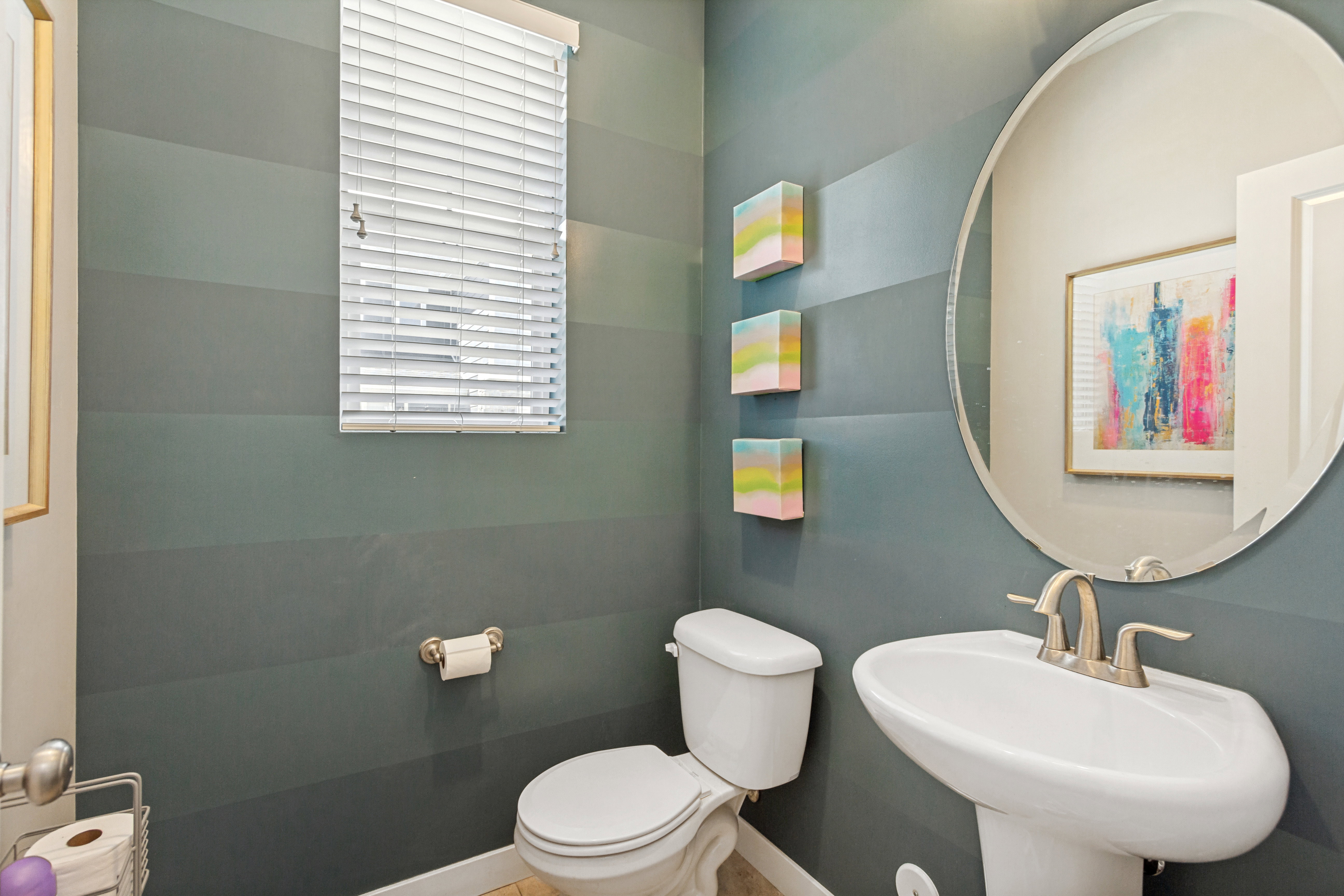 Pedestal sink with a brushed nickel faucet, complemented by a large oval mirror