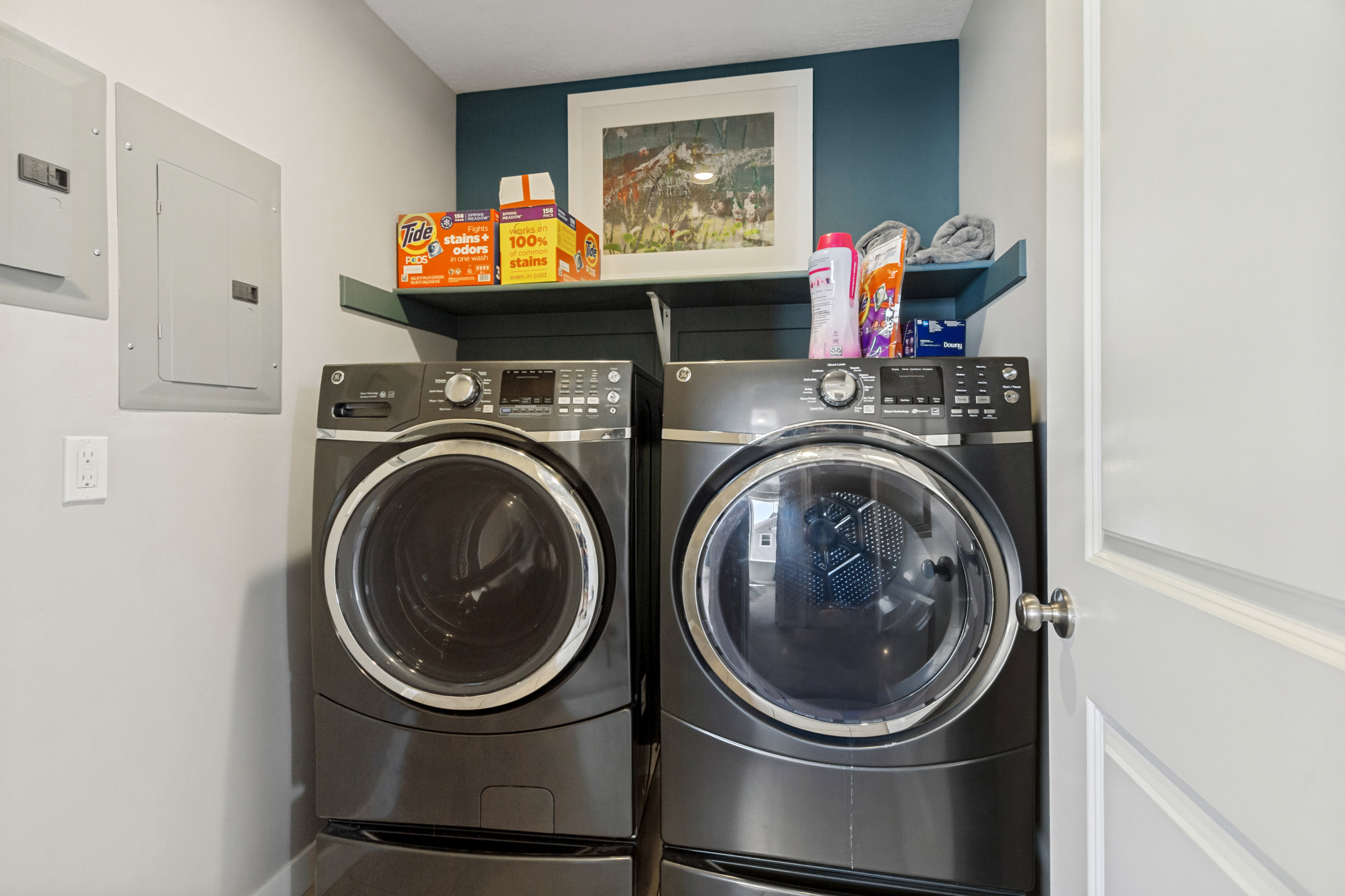 Dedicated laundry area featuring front-loading machines, built-in shelving, and a contrasting accent wall