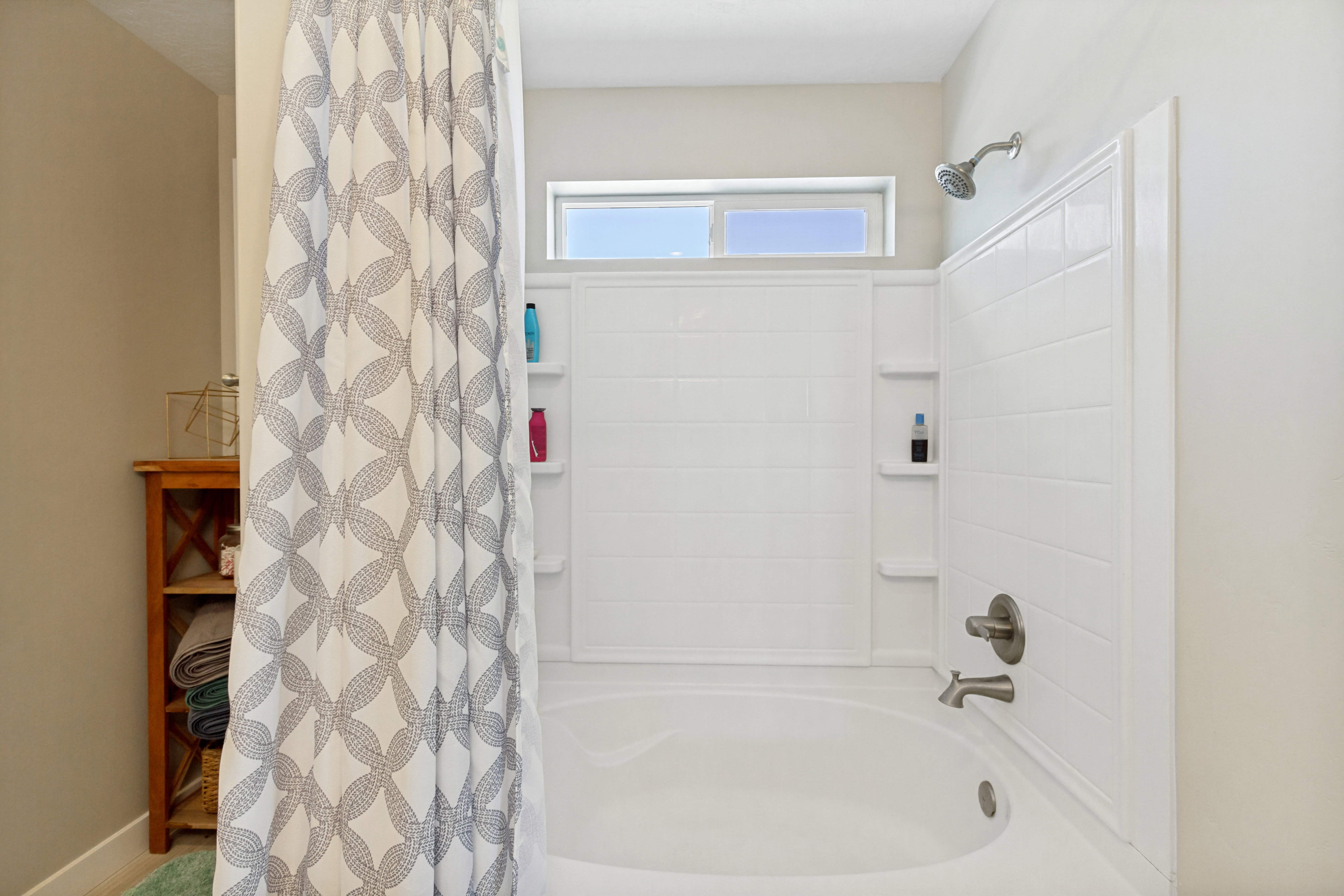 Tub and shower combination featuring white subway tile surround and integrated shelving