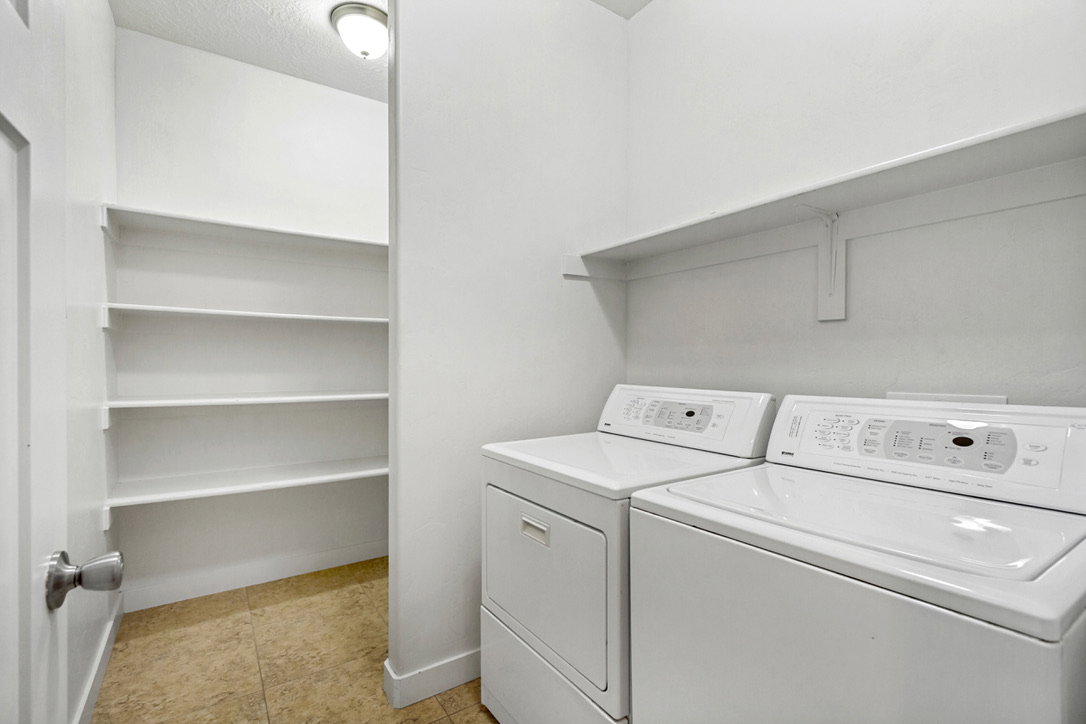 Laundry area featuring a side-by-side washer and dryer, an overhead wall-mounted shelf, and an adjacent built-in shelving unit