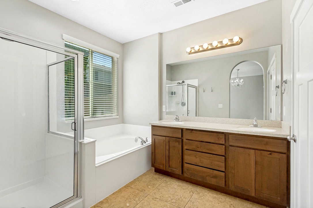 Primary bathroom featuring a double vanity with wood cabinetry and light-toned countertops, a built-in soaking tub, and a glass-enclosed shower