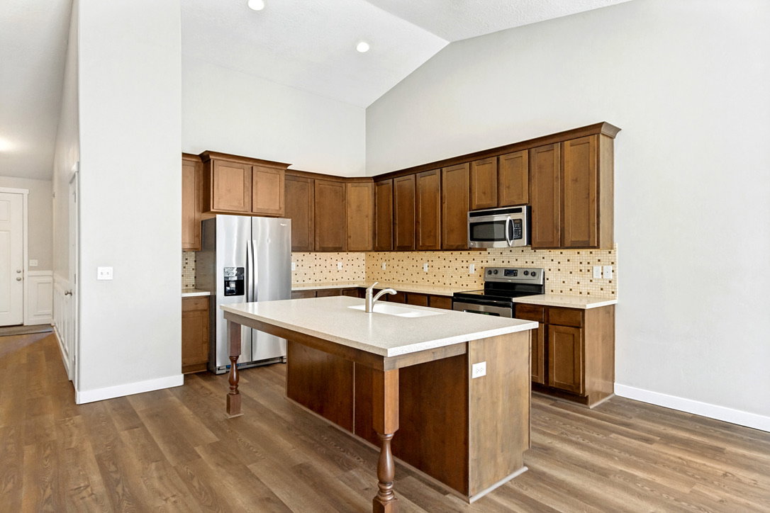 Kitchen featuring wood-finish flooring, vaulted ceiling, recessed lighting, wood cabinetry, and a central island with a light-toned countertop