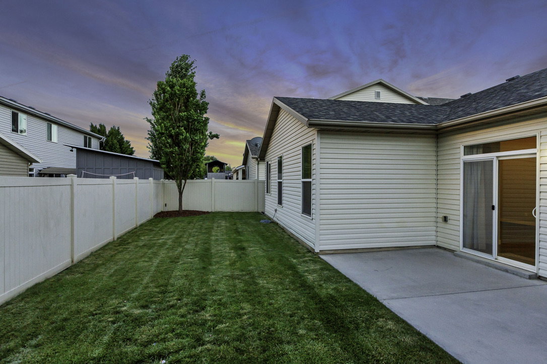 Expansive rear yard featuring a manicured lawn, established tree, and full privacy fencing