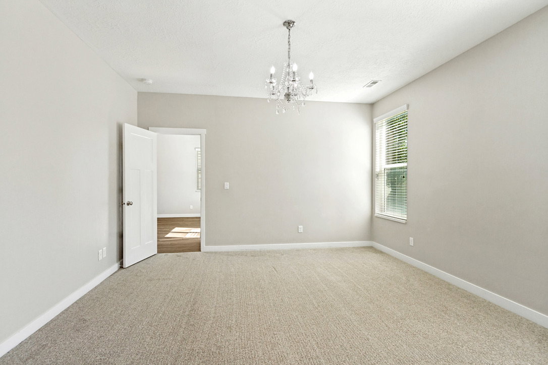 Primary bedroom is spacious room featuring neutral carpeting and light-toned walls