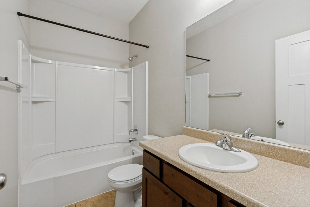 Bathroom featuring a full vanity with an integrated sink, a large wall-mounted mirror, a toilet, and a shower-tub combination with a white surround