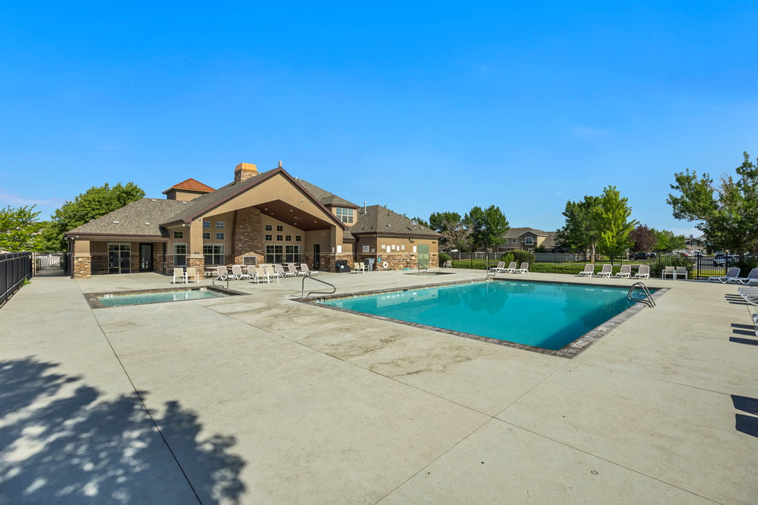 Community pool with expansive concrete decking, integrated spa, and a clubhouse featuring stone and stucco finishes