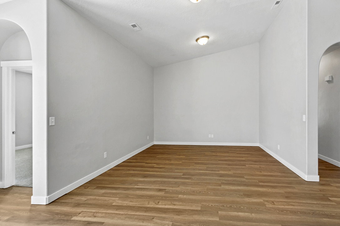 Spacious room featuring wood-finish flooring, vaulted ceilings, and a light neutral wall color