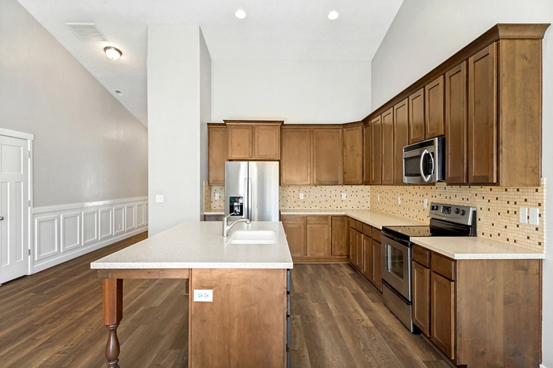 Kitchen featuring wood-finish flooring, light-toned cabinetry, stainless steel appliances, a center island with sink, and light-toned countertops