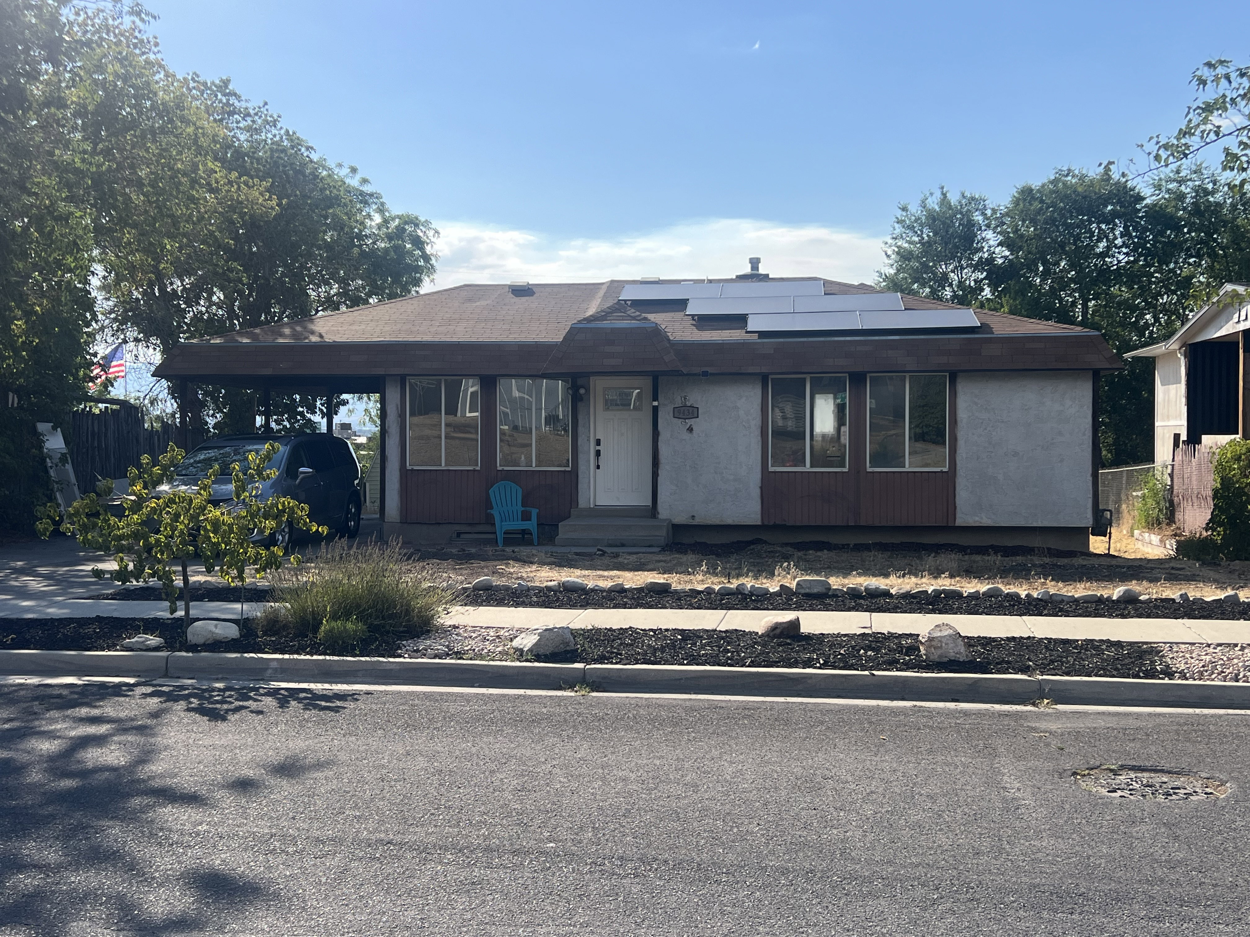 Ranch style home featuring a concrete driveway, carport, solar panels, and peach tree