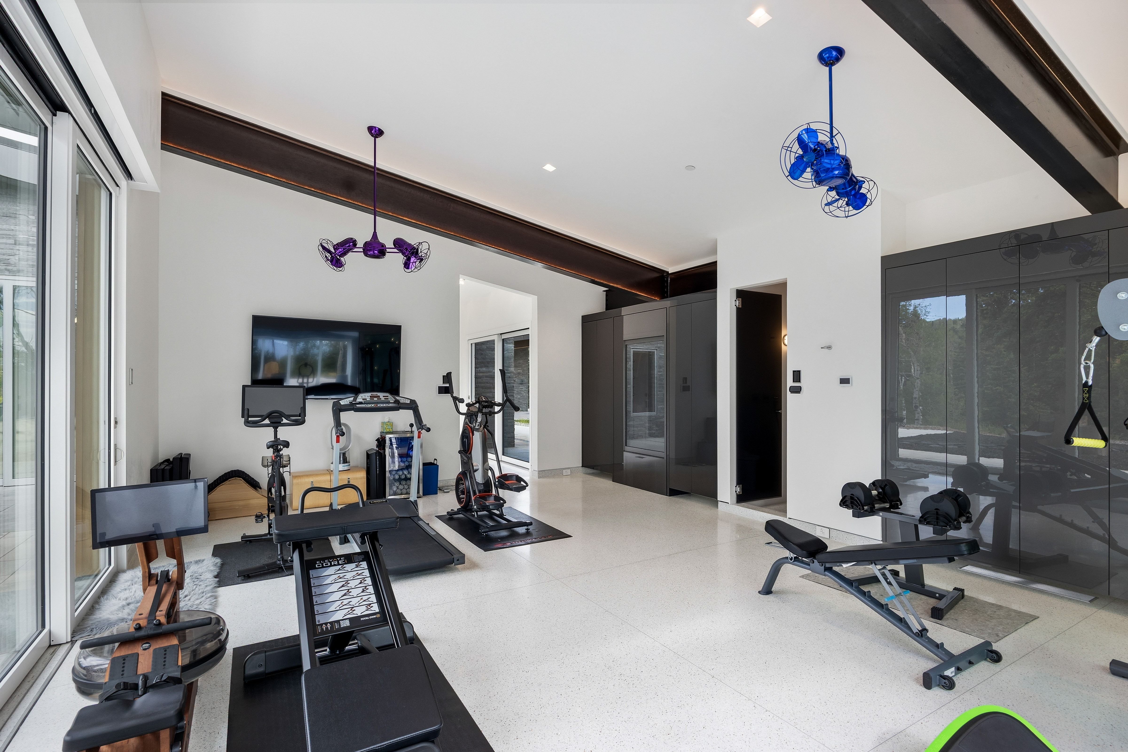 Spacious dedicated fitness area featuring high ceilings with exposed wood beams, bright recessed lighting, and large format terrazzo flooring